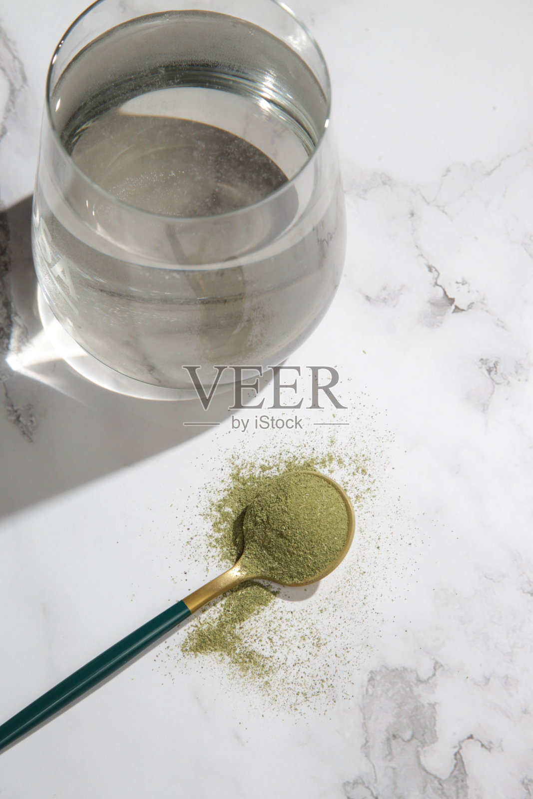 绿色粉末在勺子和一杯水。营养补充、节食、排毒、预防保健和健康生活方式的理念。照片摄影图片