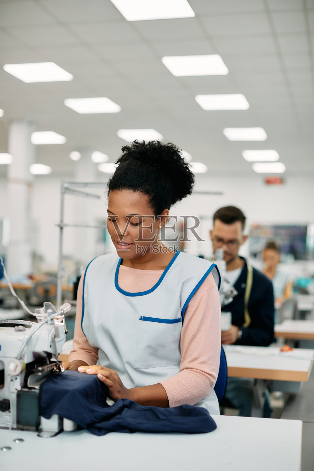 年轻的黑人妇女在纺织厂做裁缝。照片摄影图片