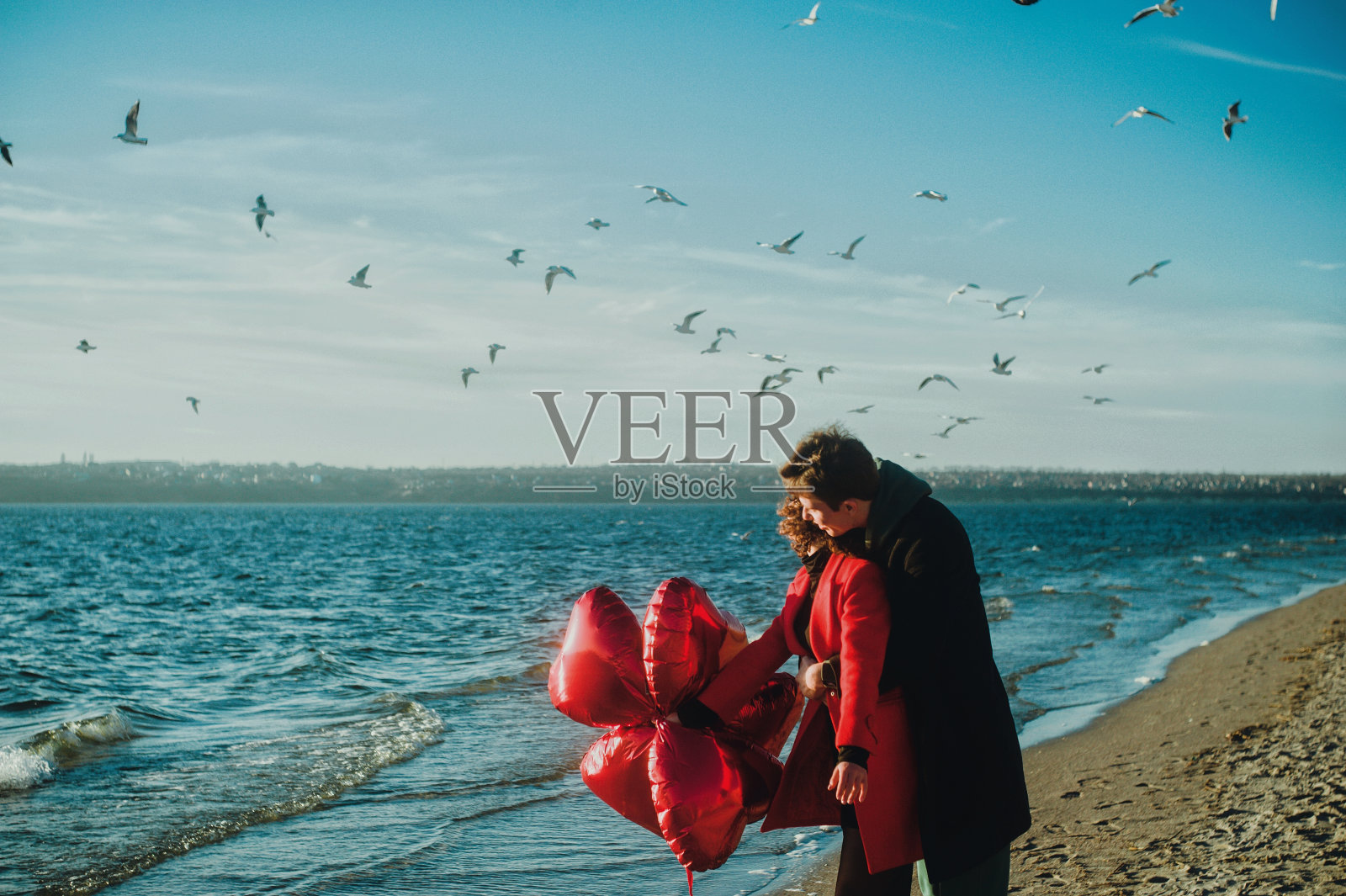 幸福微笑的情侣带着红心气球在沙滩上奔跑照片摄影图片