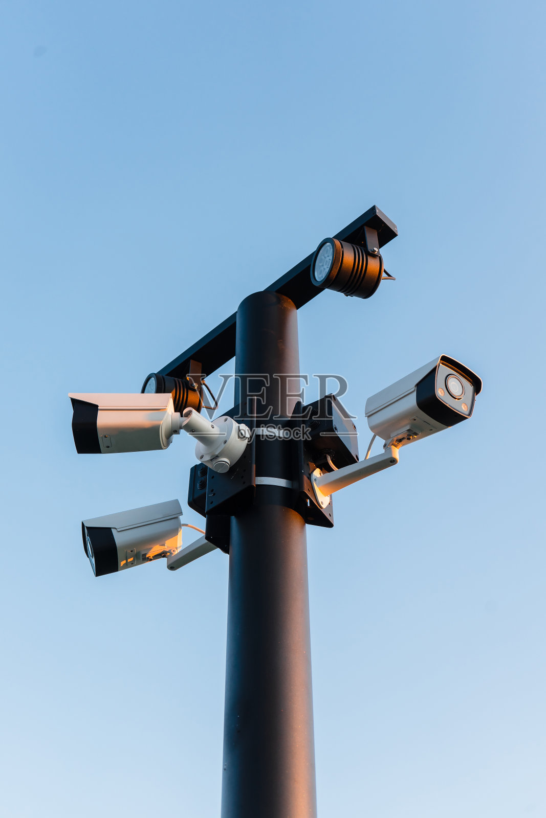 监控摄像头对准了不同方向。在晴朗的天空背景下，监控摄像头安装在高高的柱子上。照片摄影图片