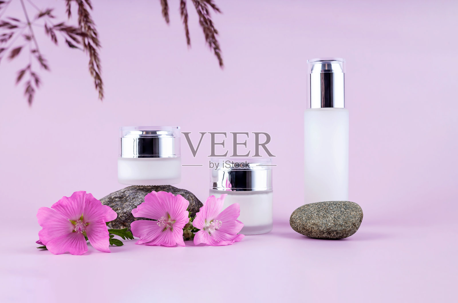 讲台上的化妆品玻璃瓶是用石头、鲜花和粉色背景上的一片草叶做成的照片摄影图片