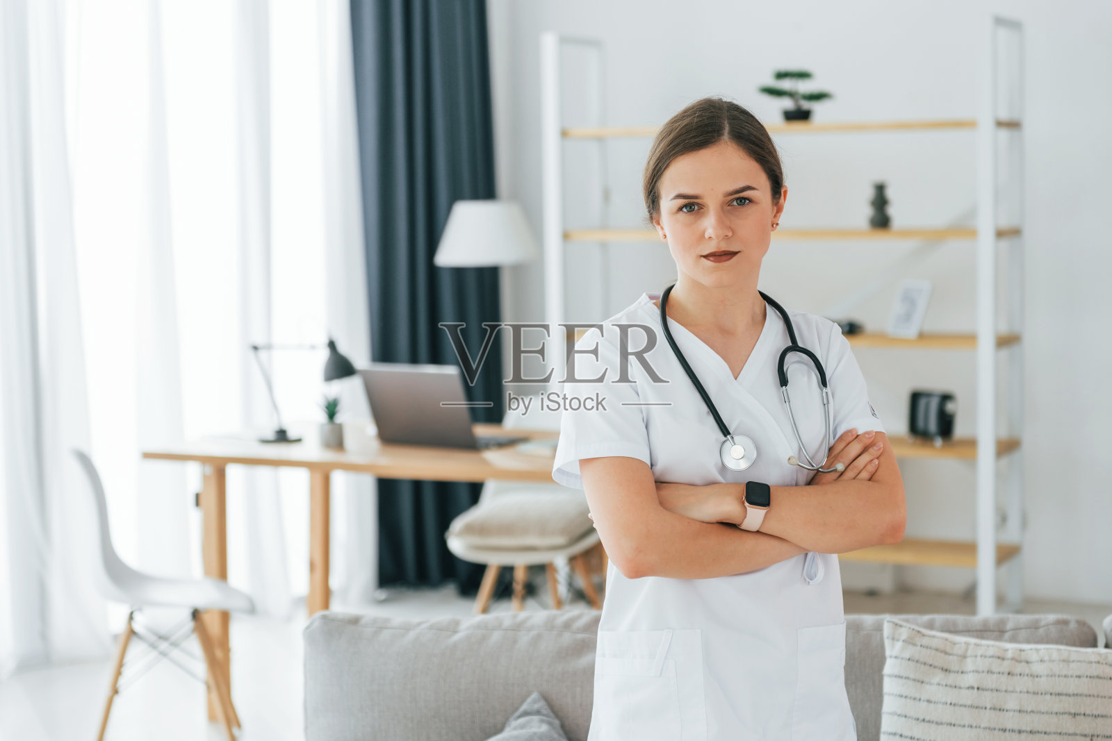 双手交叉。年轻的护士正拿着听诊器站在办公室里照片摄影图片