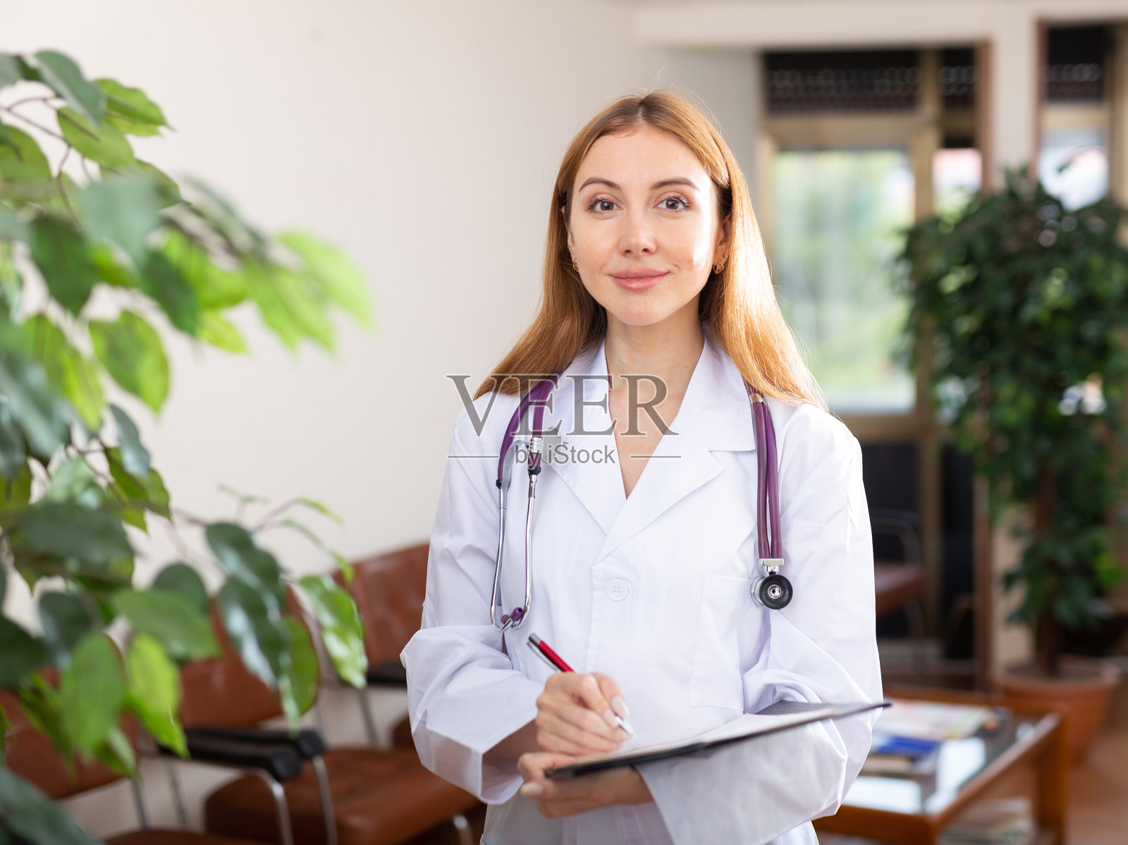 穿着白大褂的年轻女医生在写字板上填写医疗表格照片摄影图片