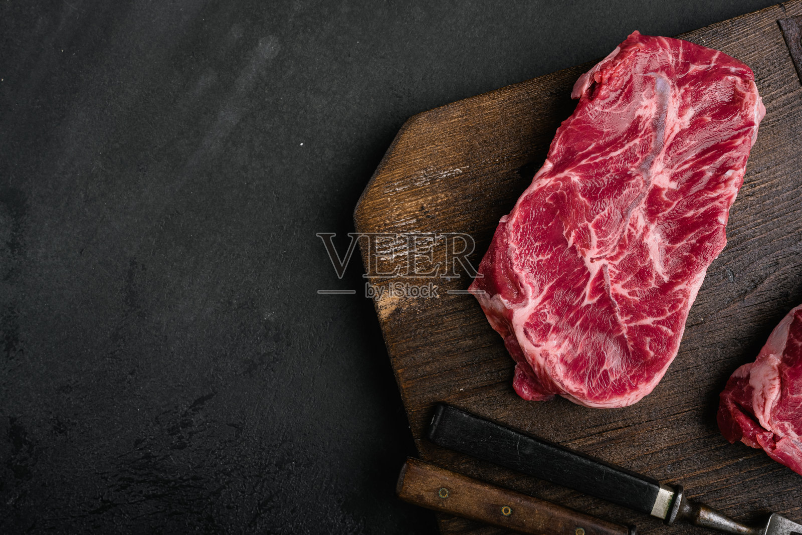 生鲜肉顶部刀片牛排，在黑色深色的石头桌子背景，顶视图平铺，与文本的复制空间照片摄影图片