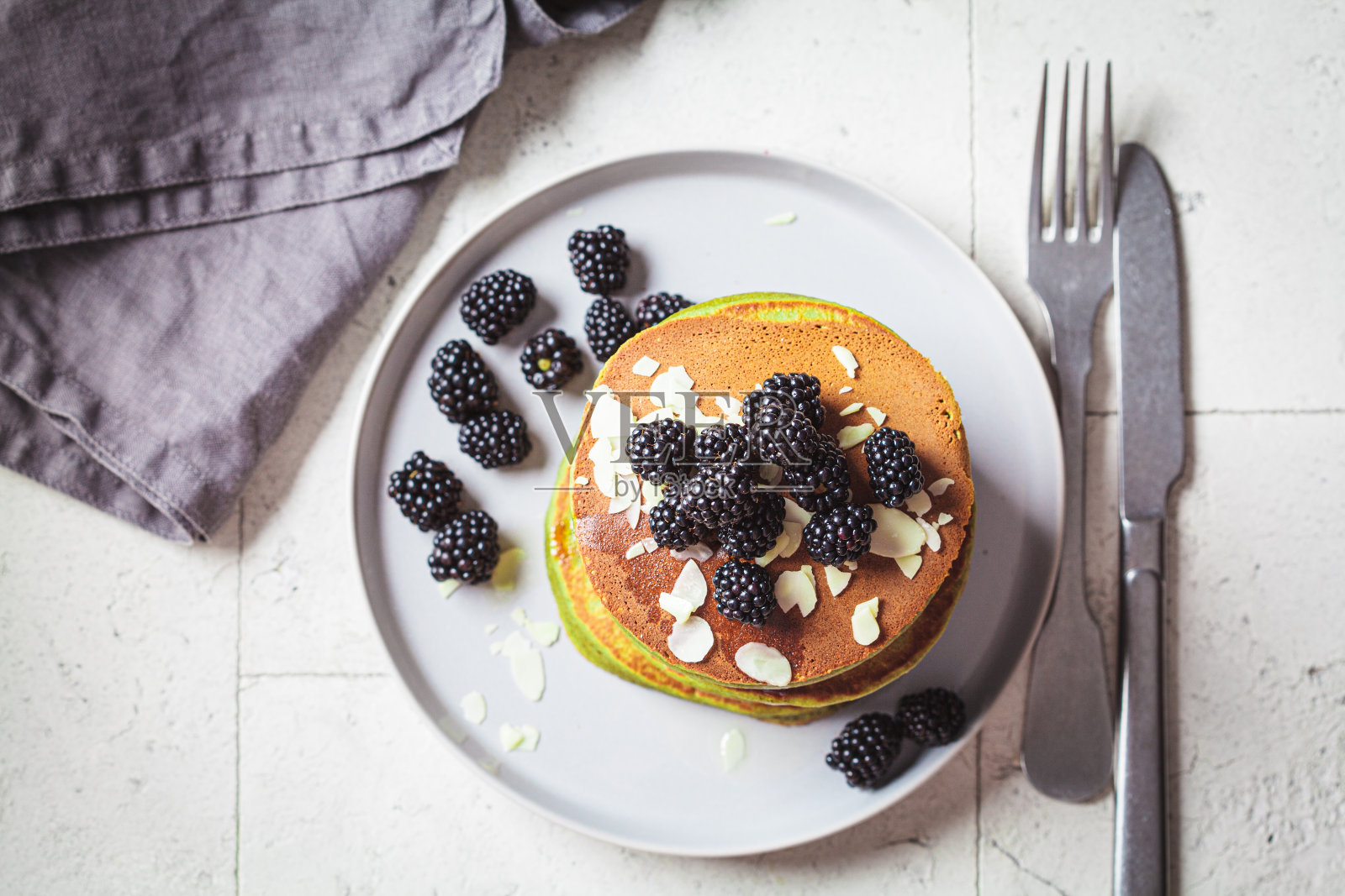素食绿色抹茶煎饼配黑莓、糖浆和杏仁。植物配方，替代食物概念。照片摄影图片