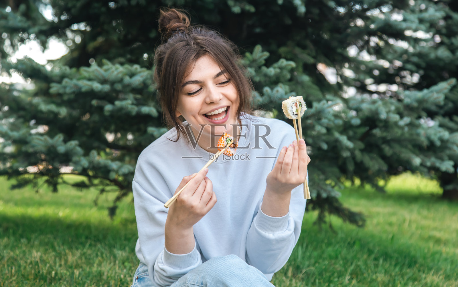 一个年轻女子在公园里吃寿司，在大自然中野餐。照片摄影图片