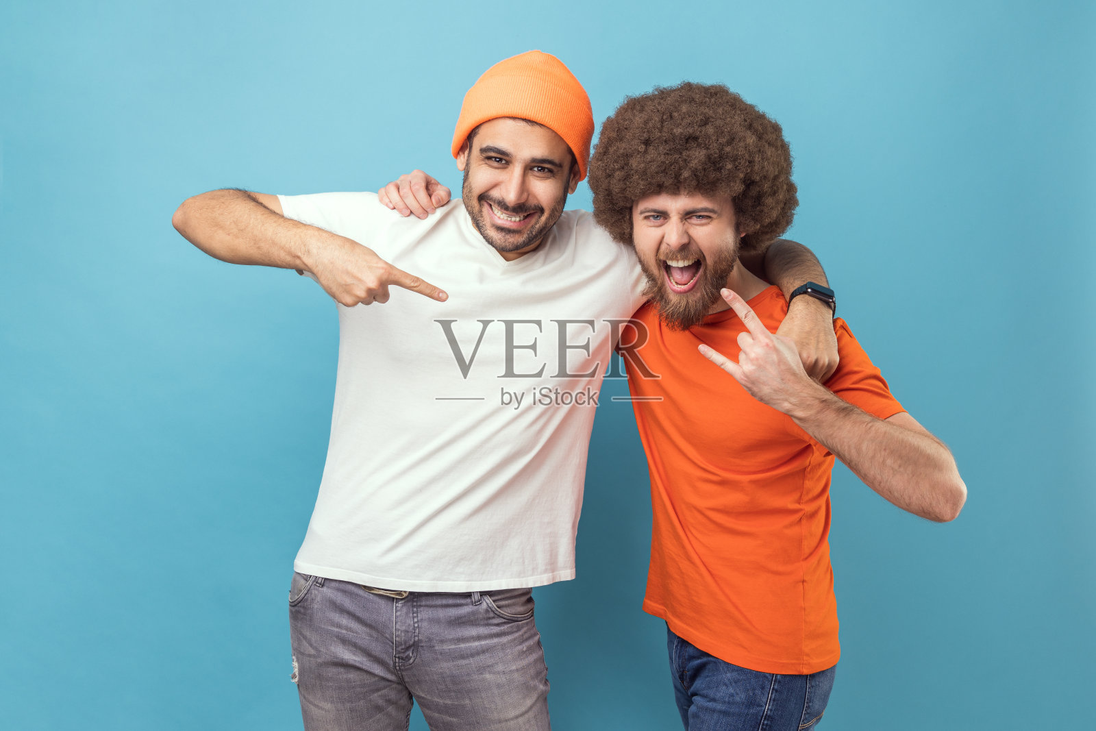 有着非洲爆炸头的男人做出摇滚手势，戴着无檐小便帽的男人指着他的朋友照片摄影图片