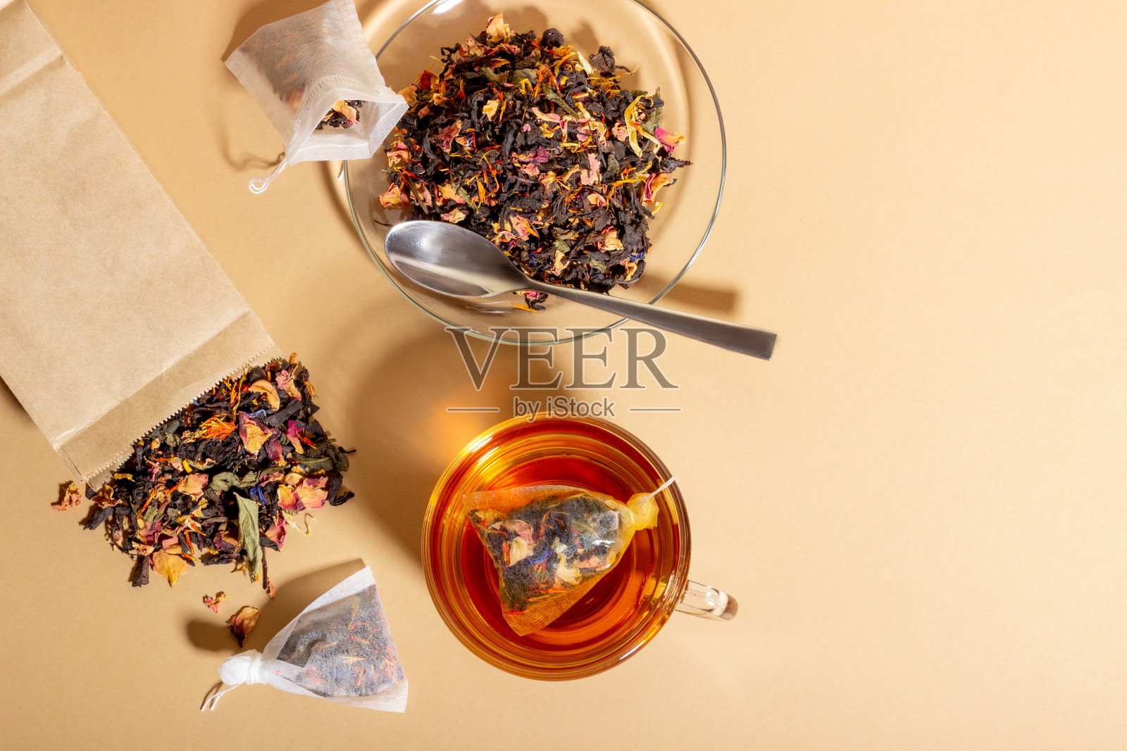 红茶，草药和水果在一个透明的杯子冲泡。用茶包冲泡的茶。天然健康饮料的理念。米色背景的茶包照片摄影图片