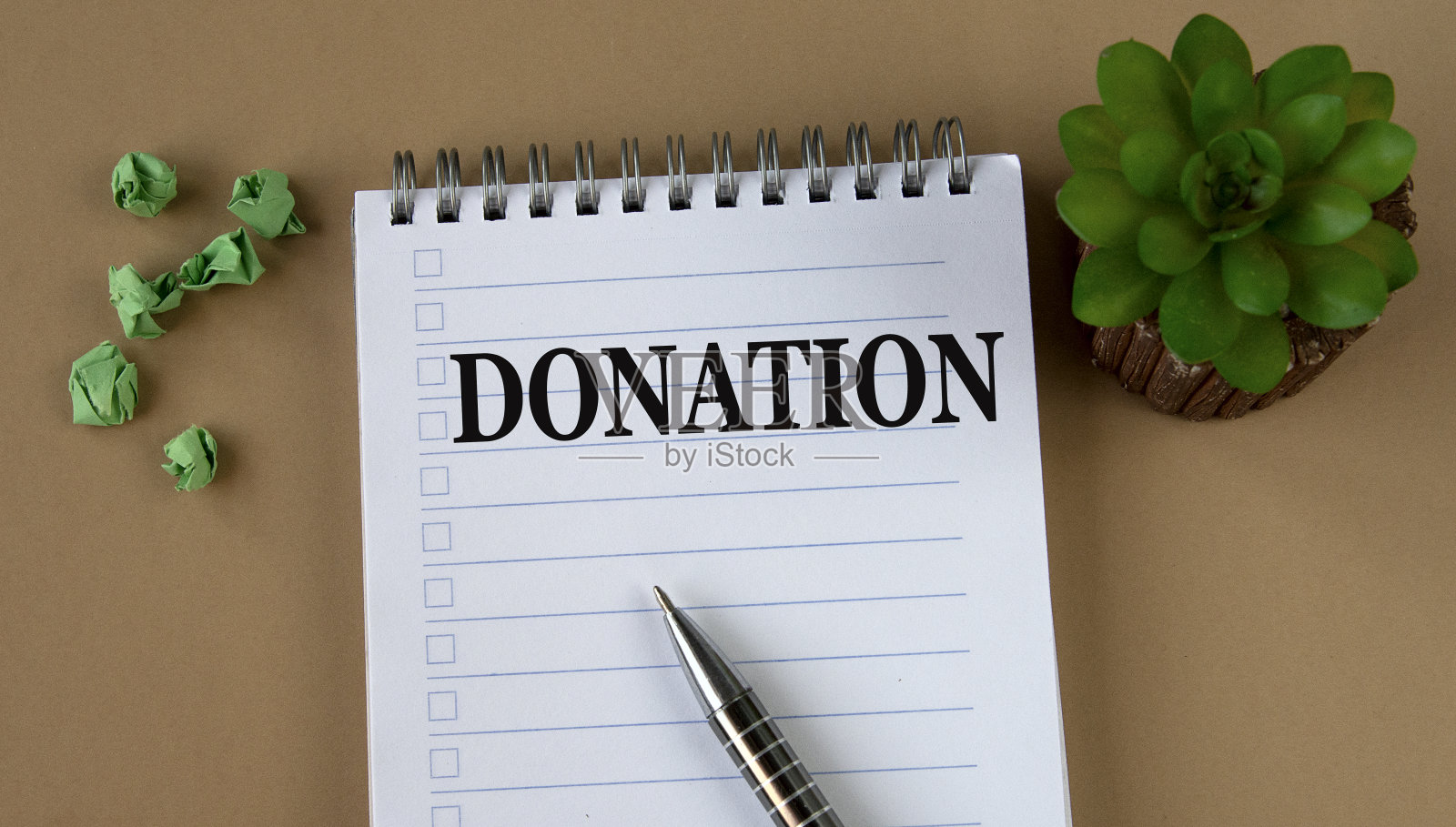 捐赠——白色笔记本上的字，背景是一棵仙人掌和皱巴巴的纸张照片摄影图片