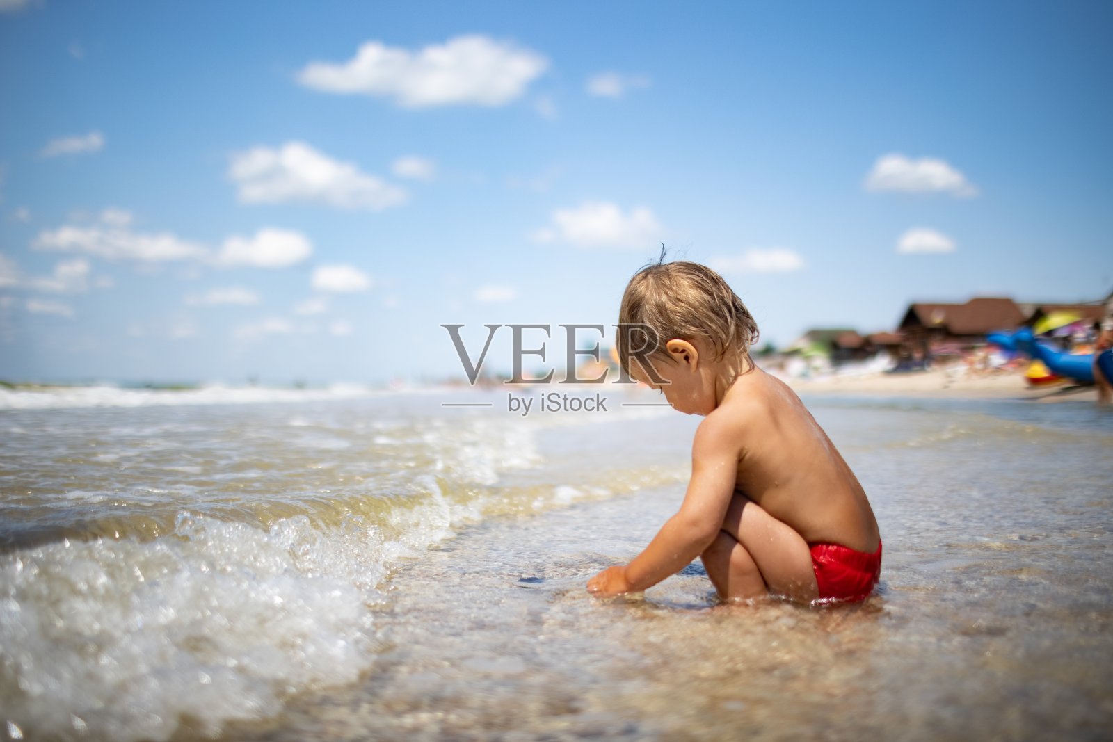 在夏日的阳光下，孩子在海边的沙滩上收集贝壳和鹅卵石照片摄影图片