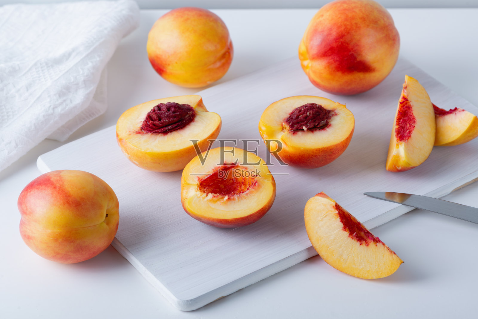 成熟多汁的油桃，整个和一半的木材砧板，刀，白色厨房毛巾，近距离，现代极简风格照片摄影图片