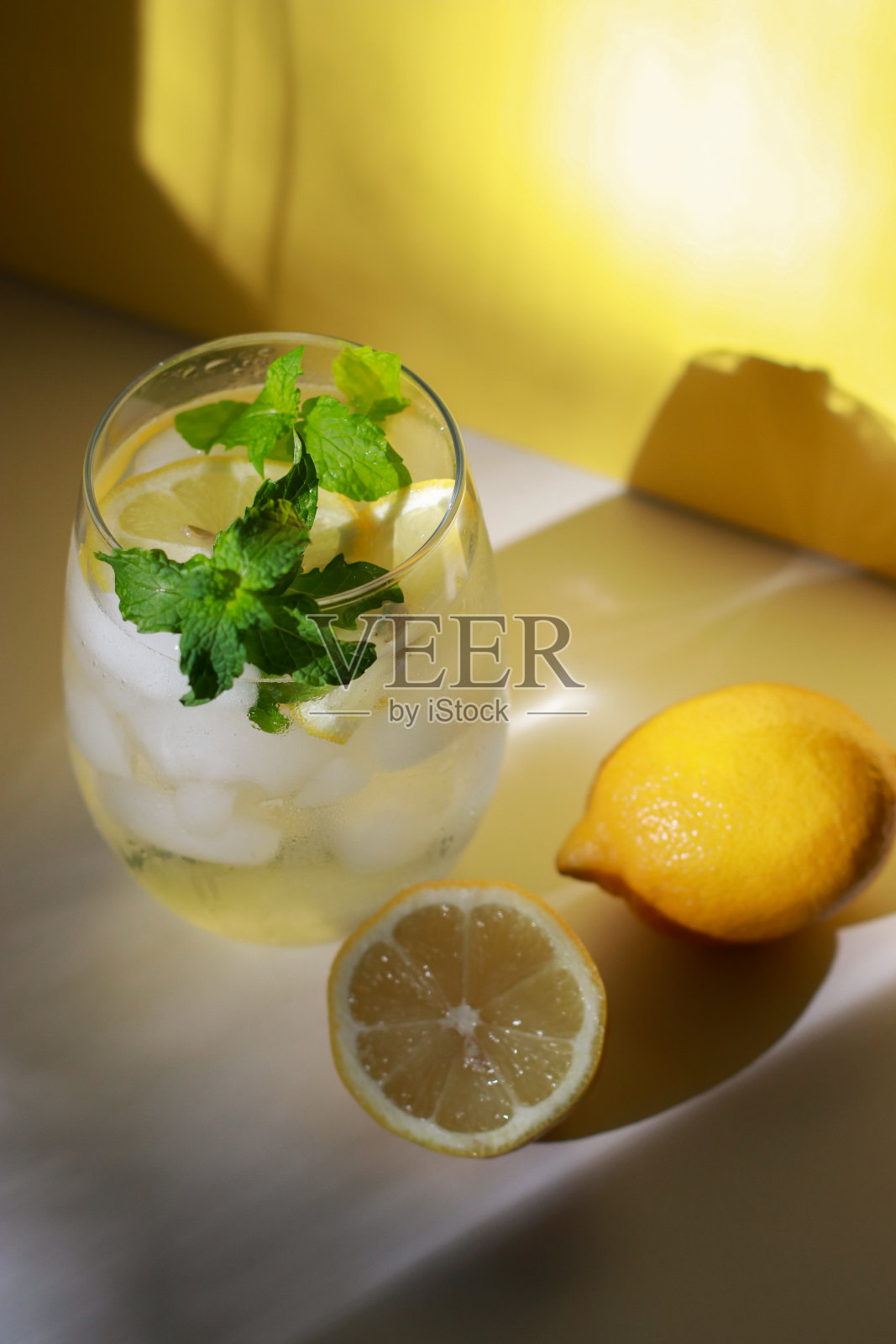 一杯水，薄荷，柠檬和冰在白色的桌子上，黄色的背景照片摄影图片