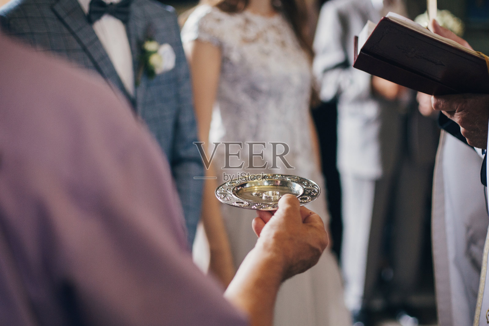 在教堂举行神圣的婚礼时，牧师手持装有时髦结婚戒指的盘子。在大教堂举行婚礼。给新娘和新郎的结婚戒指照片摄影图片