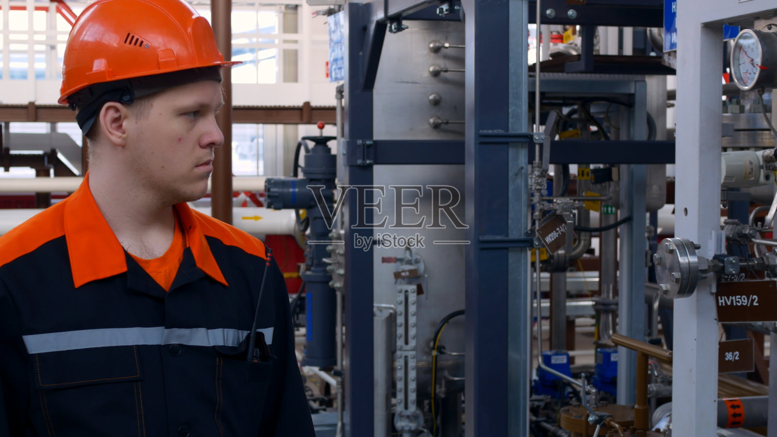 一名戴着头盔的工厂工人绕着设备走，检查它的性能。在危险场所工作。使用技术设备从事生产工作。戴着头盔，穿着工作服的机械师。照片摄影图片