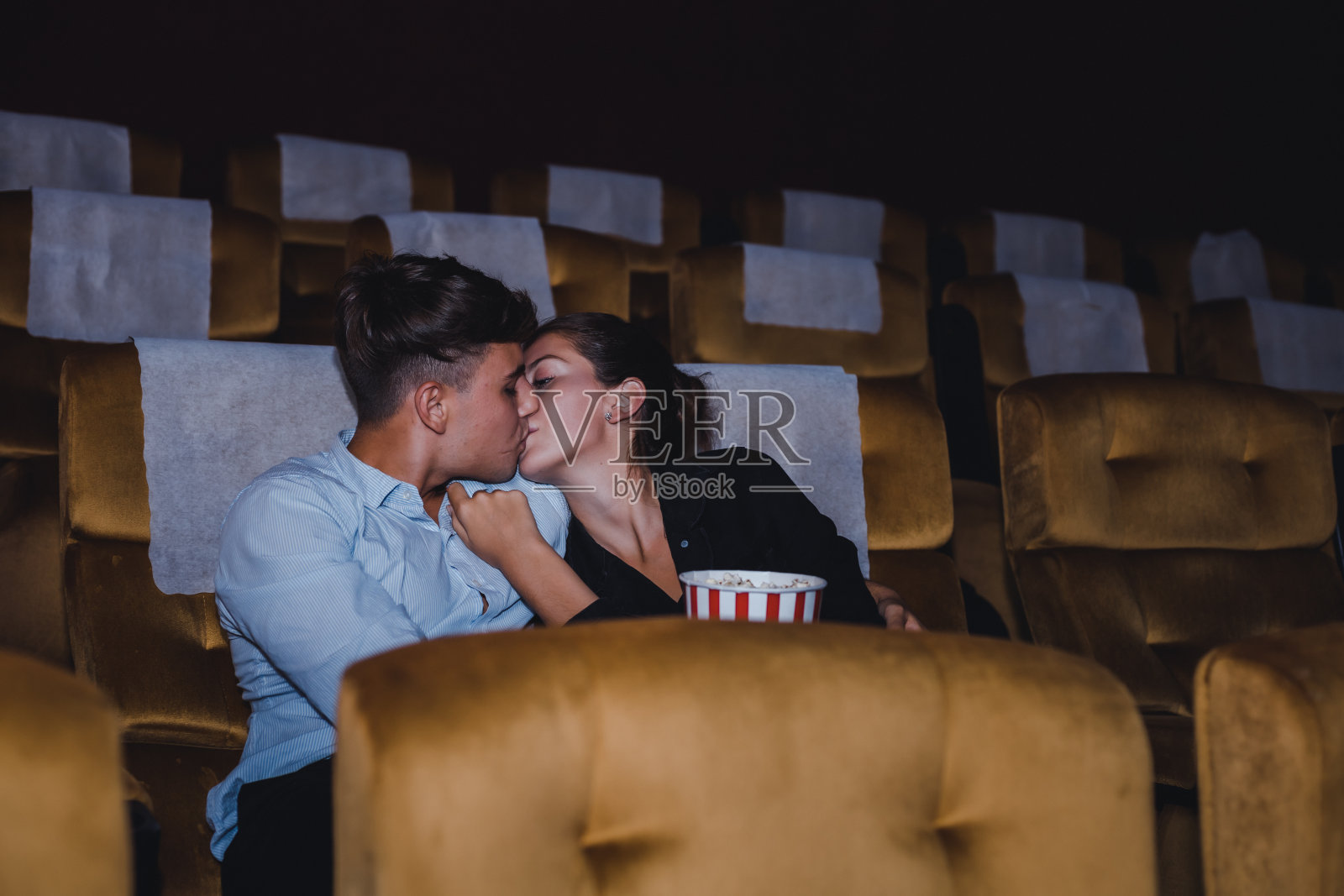 一对情侣在电影院看电影时接吻。照片摄影图片