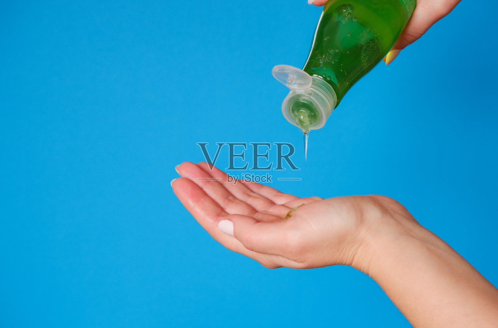 美容。一个女人把沐浴露涂在手上。绿色瓶子蓝色背景。关闭视图。照片摄影图片