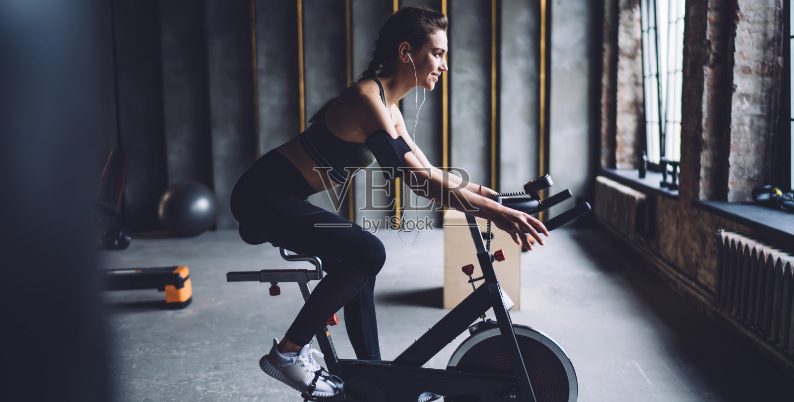 微笑的白人女性穿着运动服坐在锻炼自行车有氧锻炼听音乐，快乐的女人满意的声音配件娱乐训练期间播放列表歌曲照片摄影图片