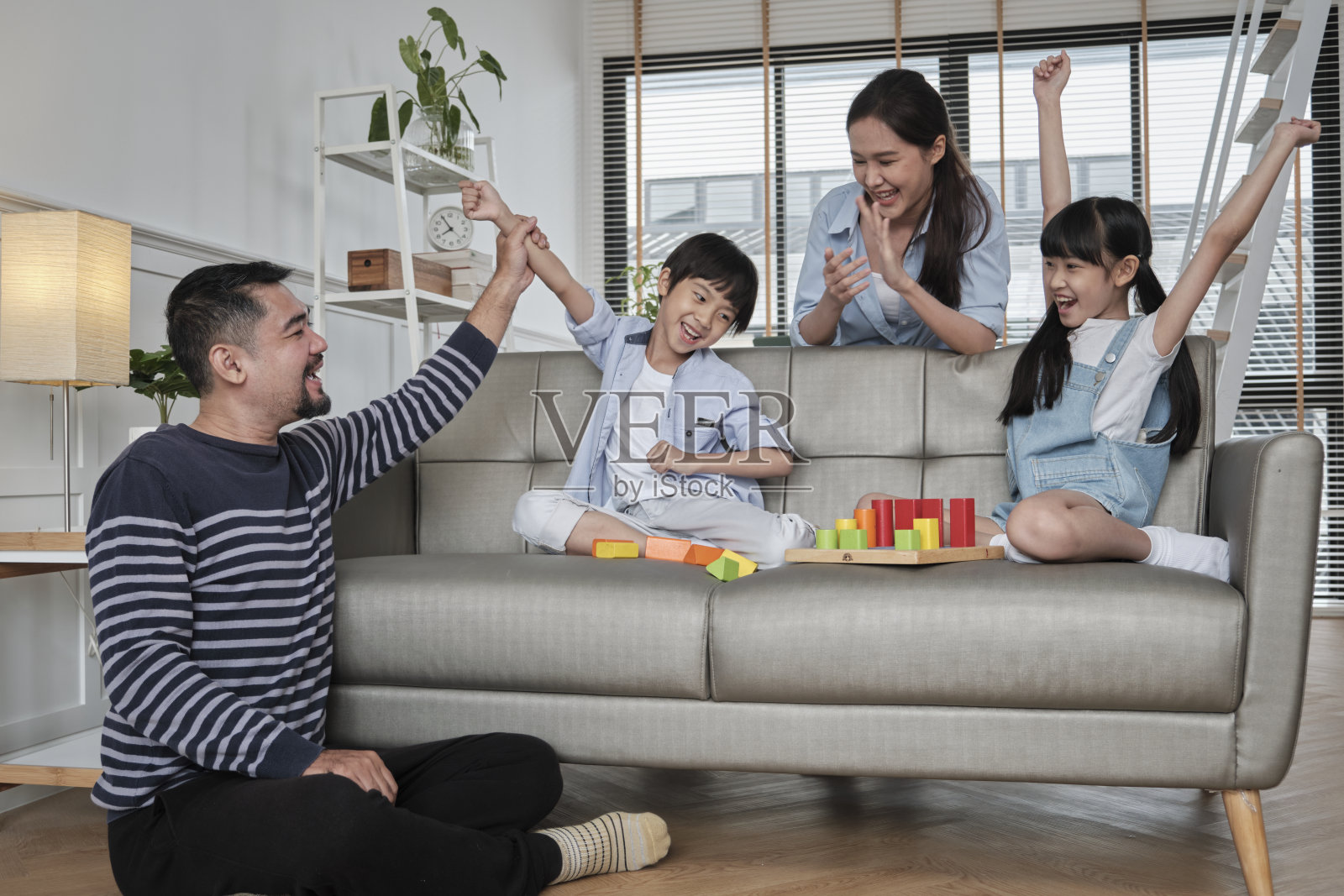 幸福的亚洲家庭，父母和孩子一起在沙发上玩五颜六色的玩具。照片摄影图片