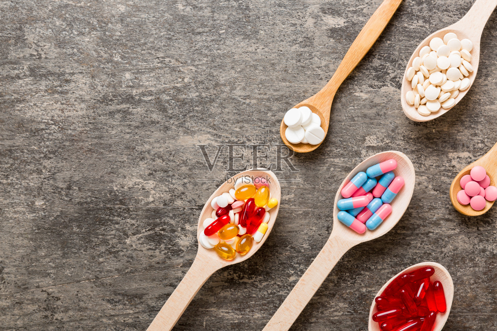 在彩色背景的勺子里装着维生素胶囊。药片作为健康的一餐。红色软凝胶维生素补充胶囊勺照片摄影图片