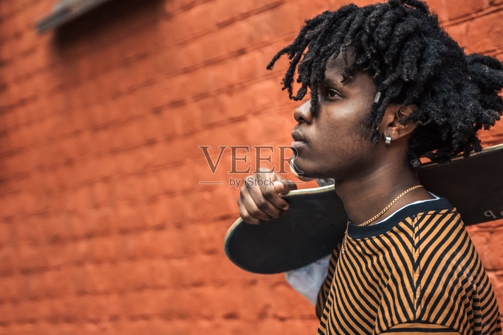 年轻英俊时髦的非洲人，男人，肖像。自然的头发长发绺。区，街头有艺术涂鸦的城市文化。美国人用滑板玩滑板。千禧,放大镜,Y一代,Z照片摄影图片