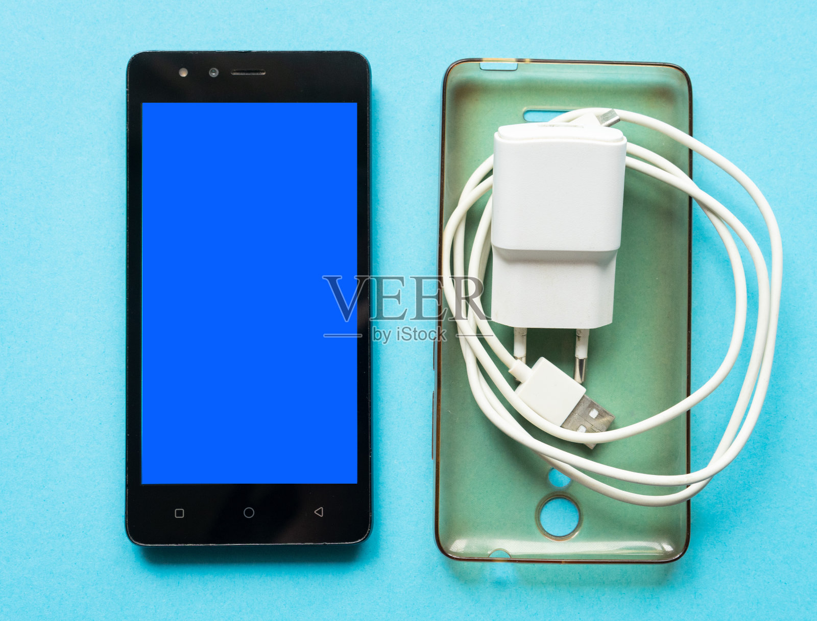 蓝色背景蓝屏的黑色智能手机。硅胶透明外壳和智能手机充电器。副本的空间。智能手机配件。照片摄影图片