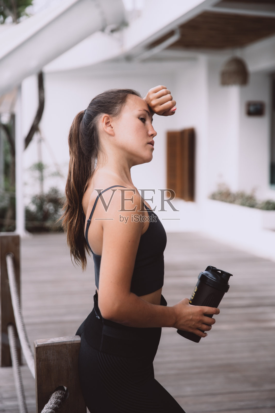 疲惫的女人在锻炼后站着休息，拿着一瓶水照片摄影图片