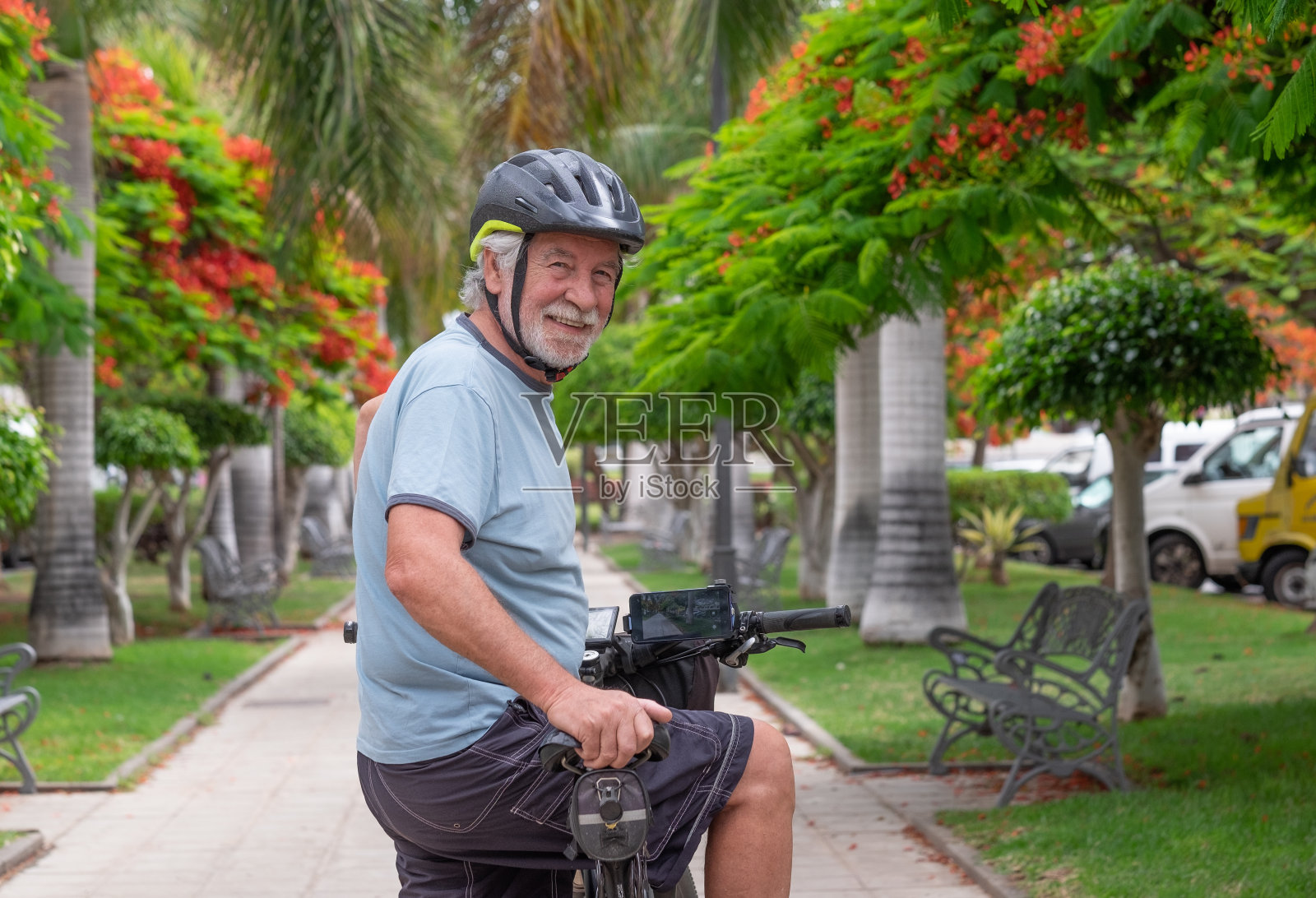 快乐活跃的老年男子骑着电动自行车在公园回头看镜头。健康生活方式和可持续移动的概念照片摄影图片