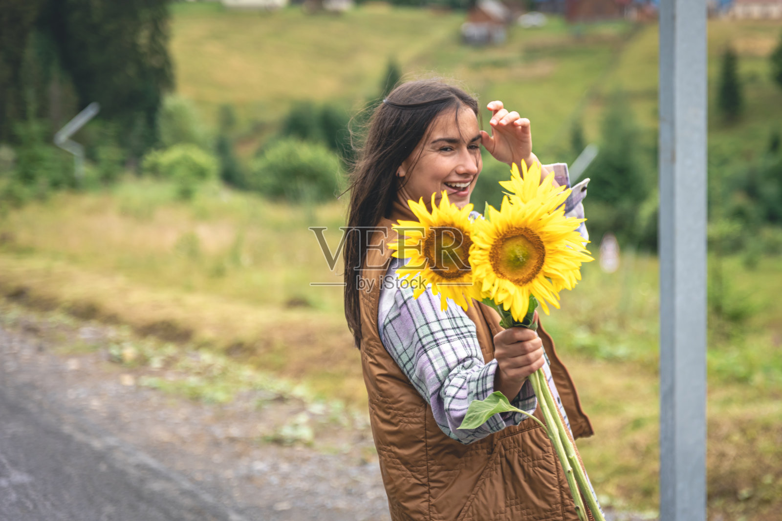 一个年轻的女人带着一束向日葵走在山里。照片摄影图片
