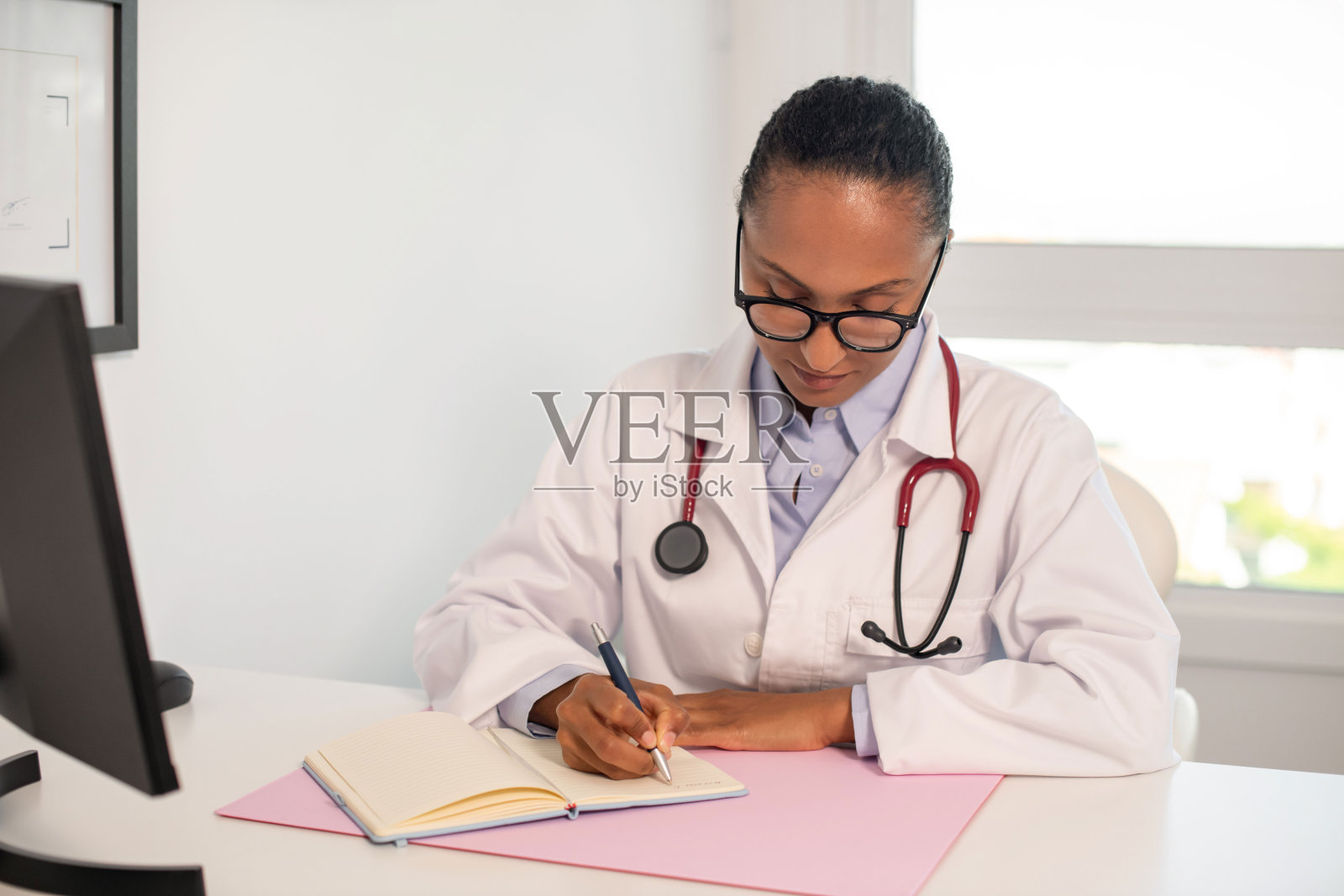 微笑的女医生在办公室笔记本上写字的肖像照片摄影图片