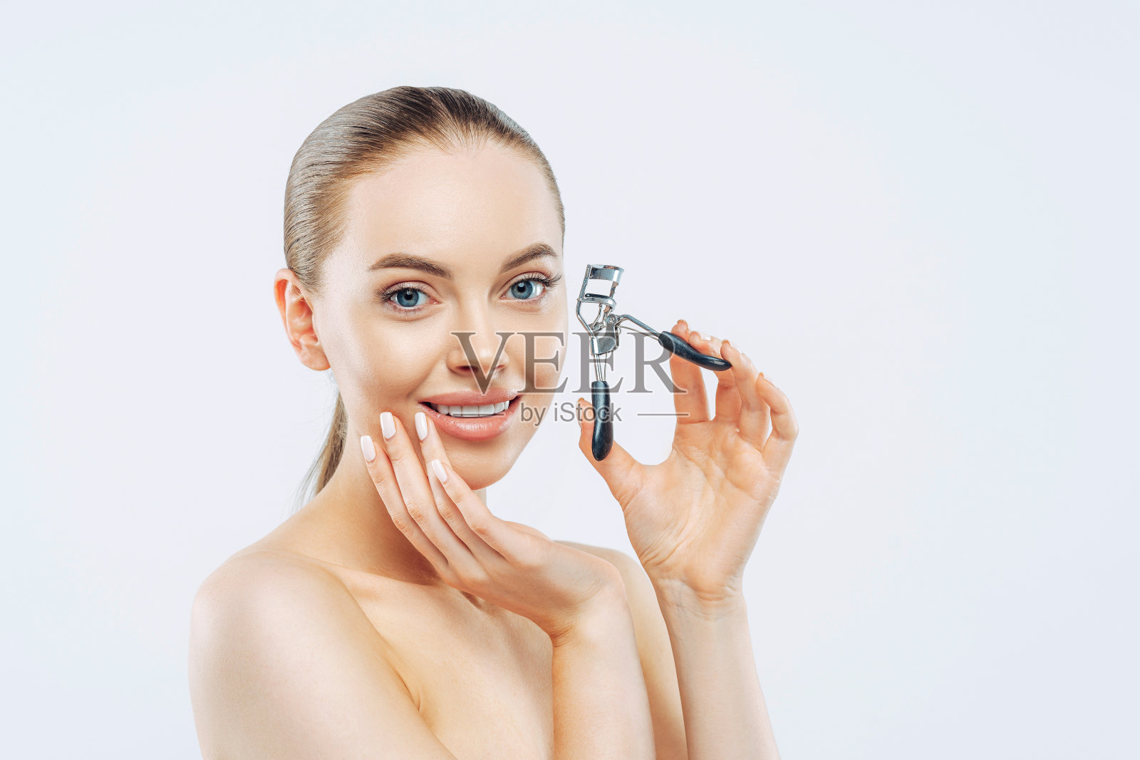 工作室拍摄的年轻黑发女子温柔微笑，使用睫毛夹，光滑柔软的皮肤，站立，有自然的妆容，触摸脸，在白色背景下的姿势。高分辨率照片摄影图片