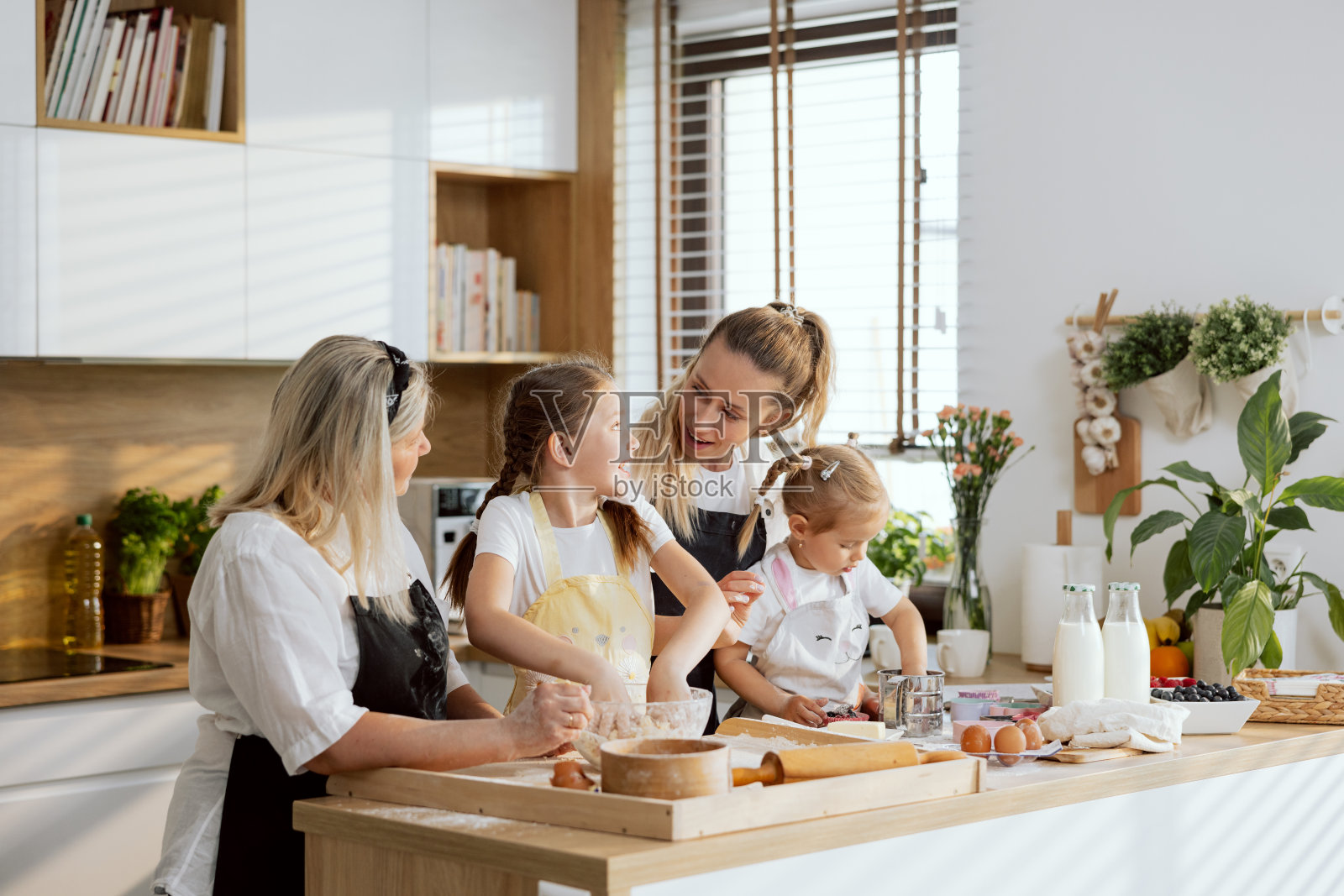 妈妈和奶奶兴奋地看着揉面过程。大女孩女主准备自制面团烹饪纸杯蛋糕饼干。学龄前的女儿用浆果装饰松饼照片摄影图片