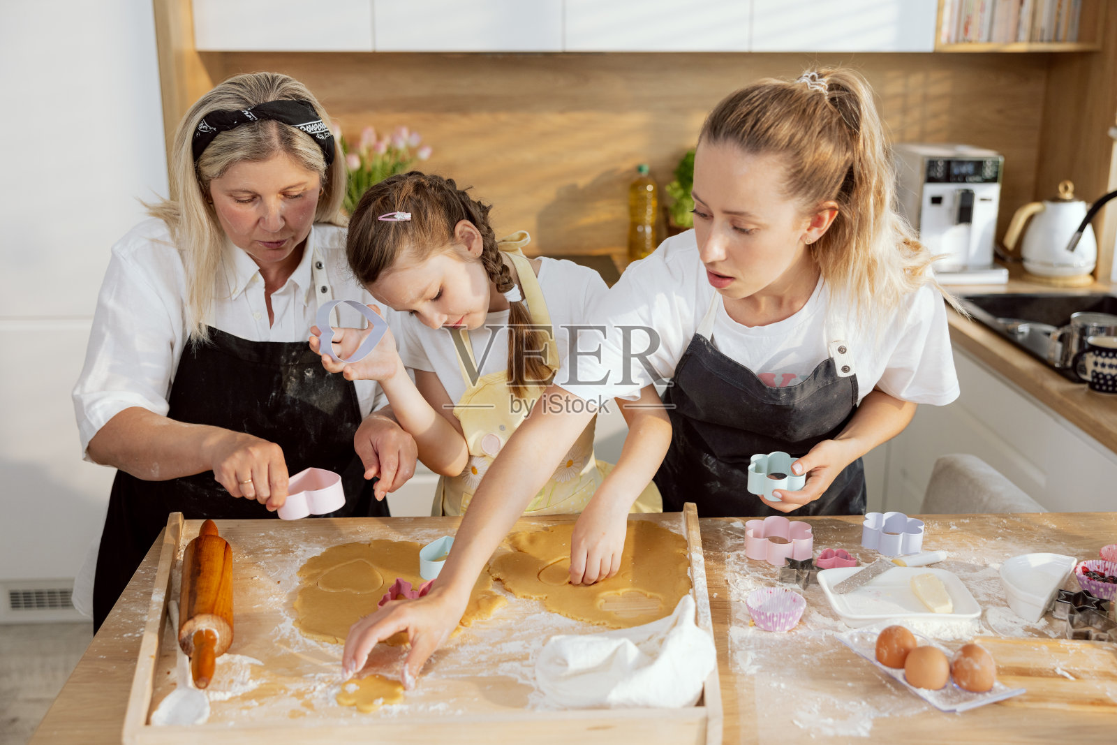 可爱的孙女手里拿着心形的饼干切割机，帮奶奶切饼干。家庭参与过程烘焙烹饪现代漂亮的厨房照片摄影图片