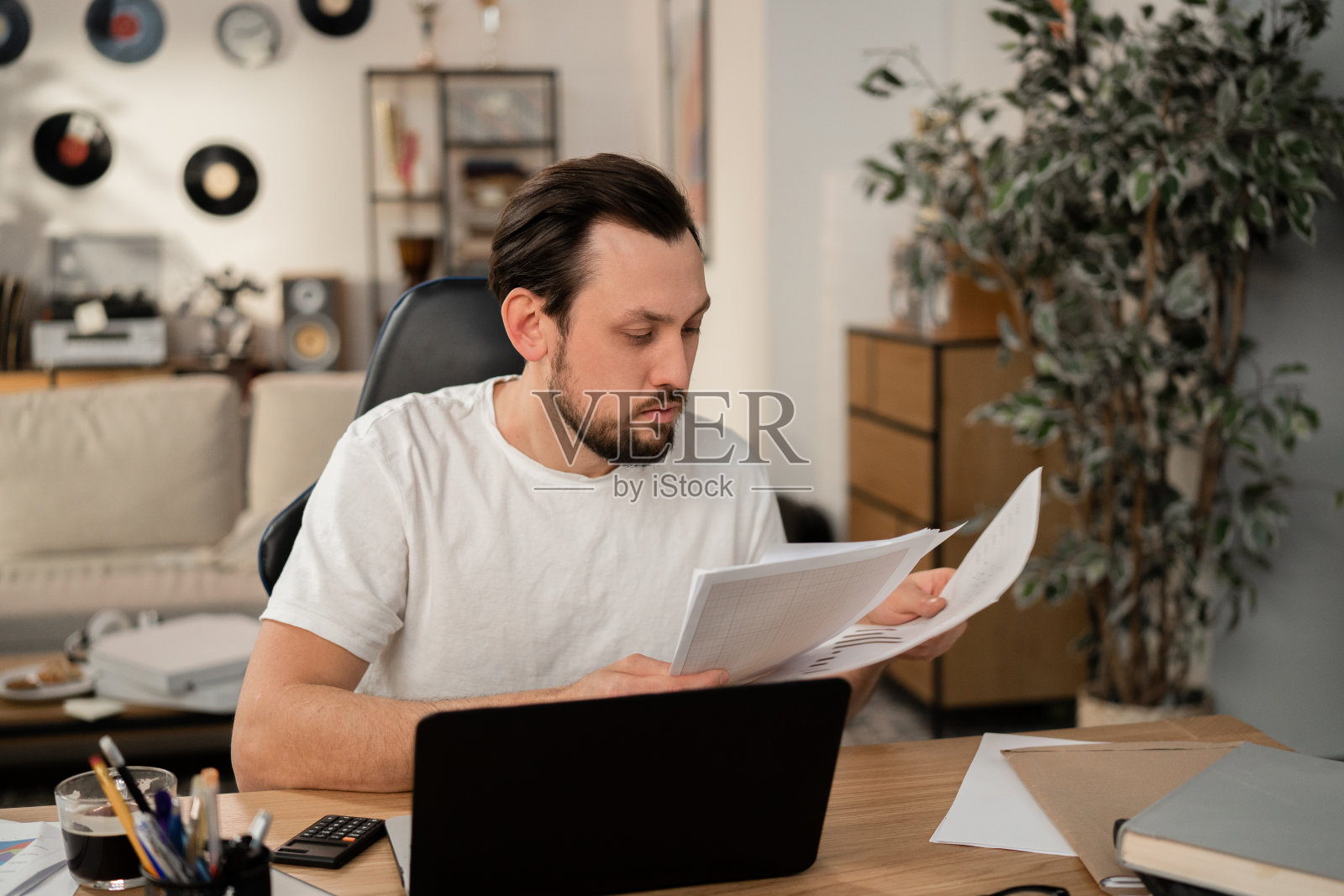 年轻的商人拿着他收到的文件，仔细地阅读。桌子上有一台打开的笔记本电脑，年轻人正在里面工作。旁边是一杯咖啡和计算器照片摄影图片