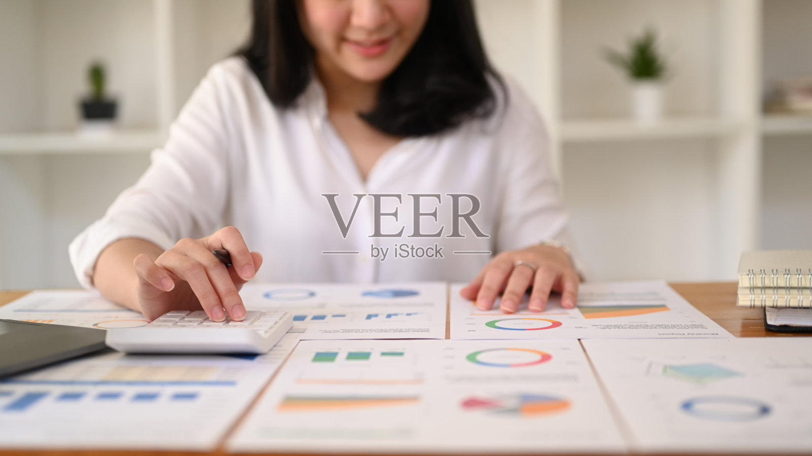 年轻的女商人在现代工作场所使用笔记本电脑和处理财务文件。照片摄影图片