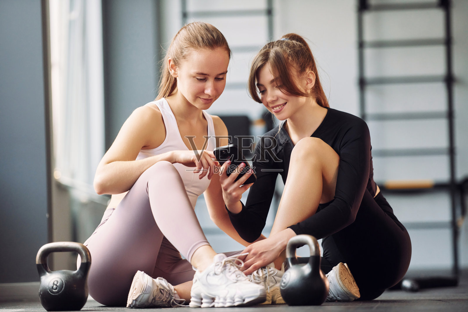 坐着休息一下。两个穿着运动服的女人一起在健身房健身照片摄影图片