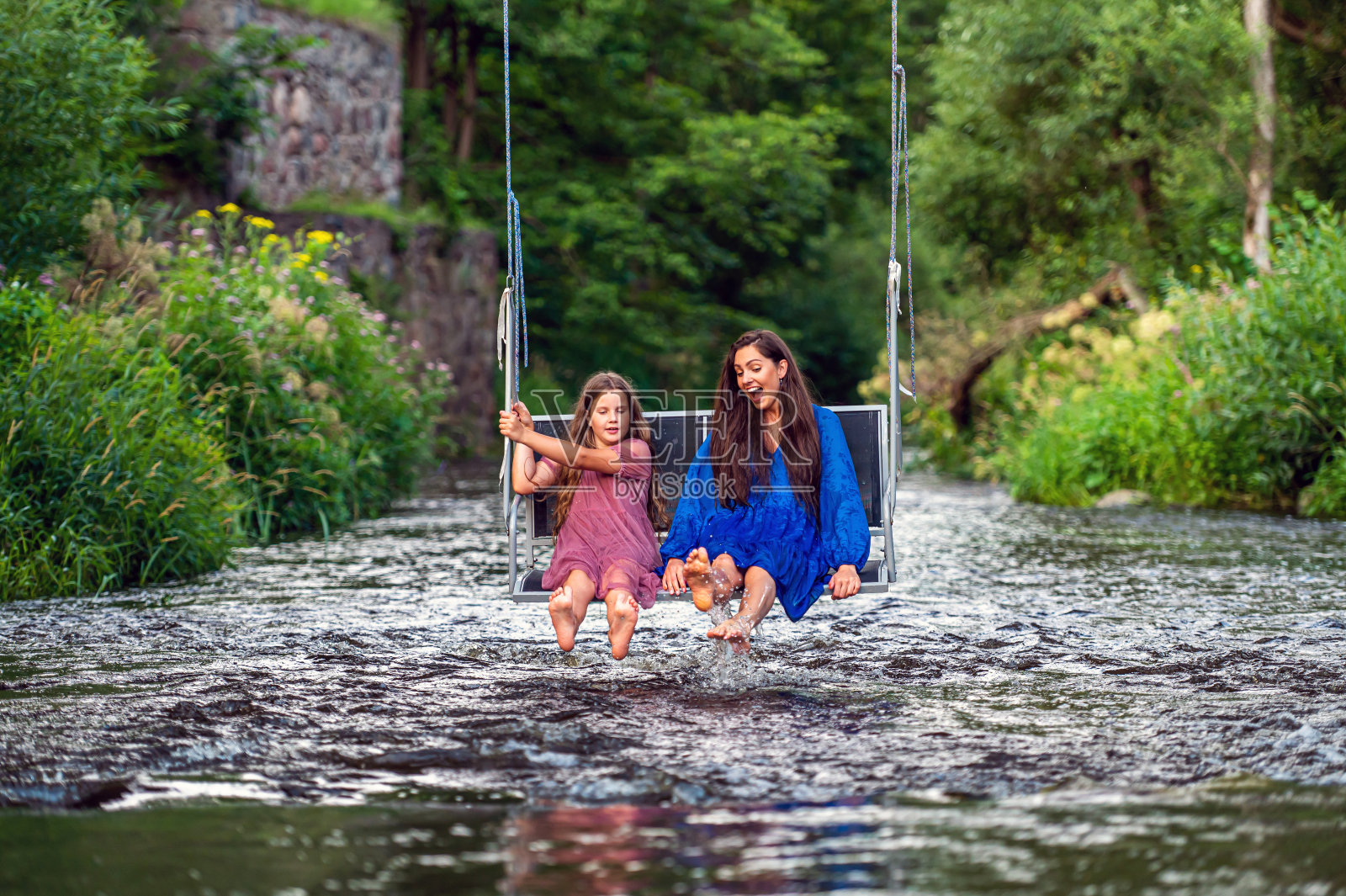 一个女人和一个小女孩在湍急的河流上荡秋千，笑着，溅起水花照片摄影图片
