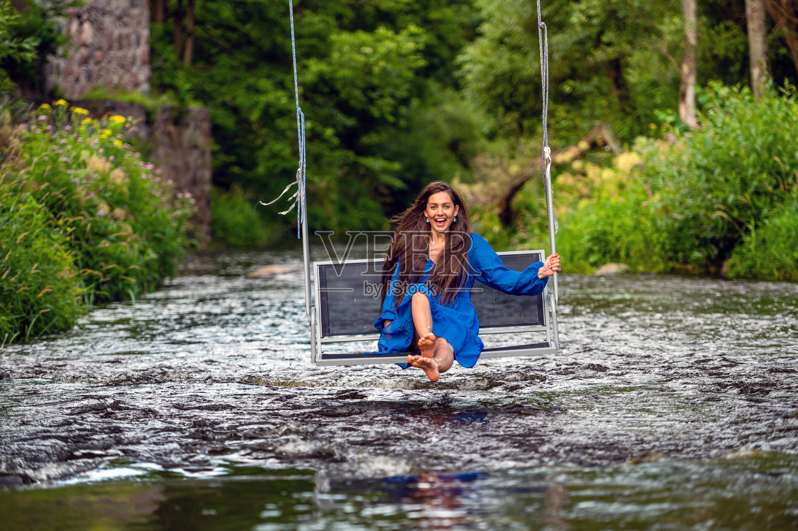 一个快乐的年轻女子在一根秋千上荡过湍急的河流照片摄影图片