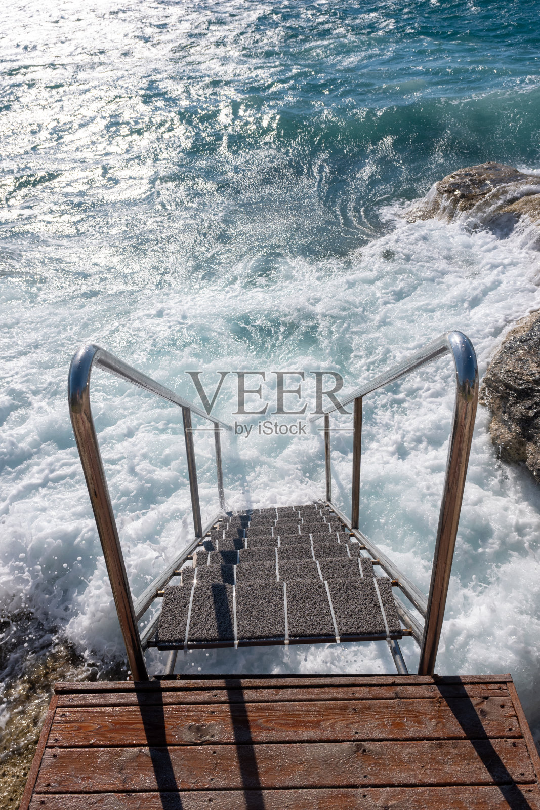 有扶手的梯子，供人从多石的海岸下到海里游泳照片摄影图片