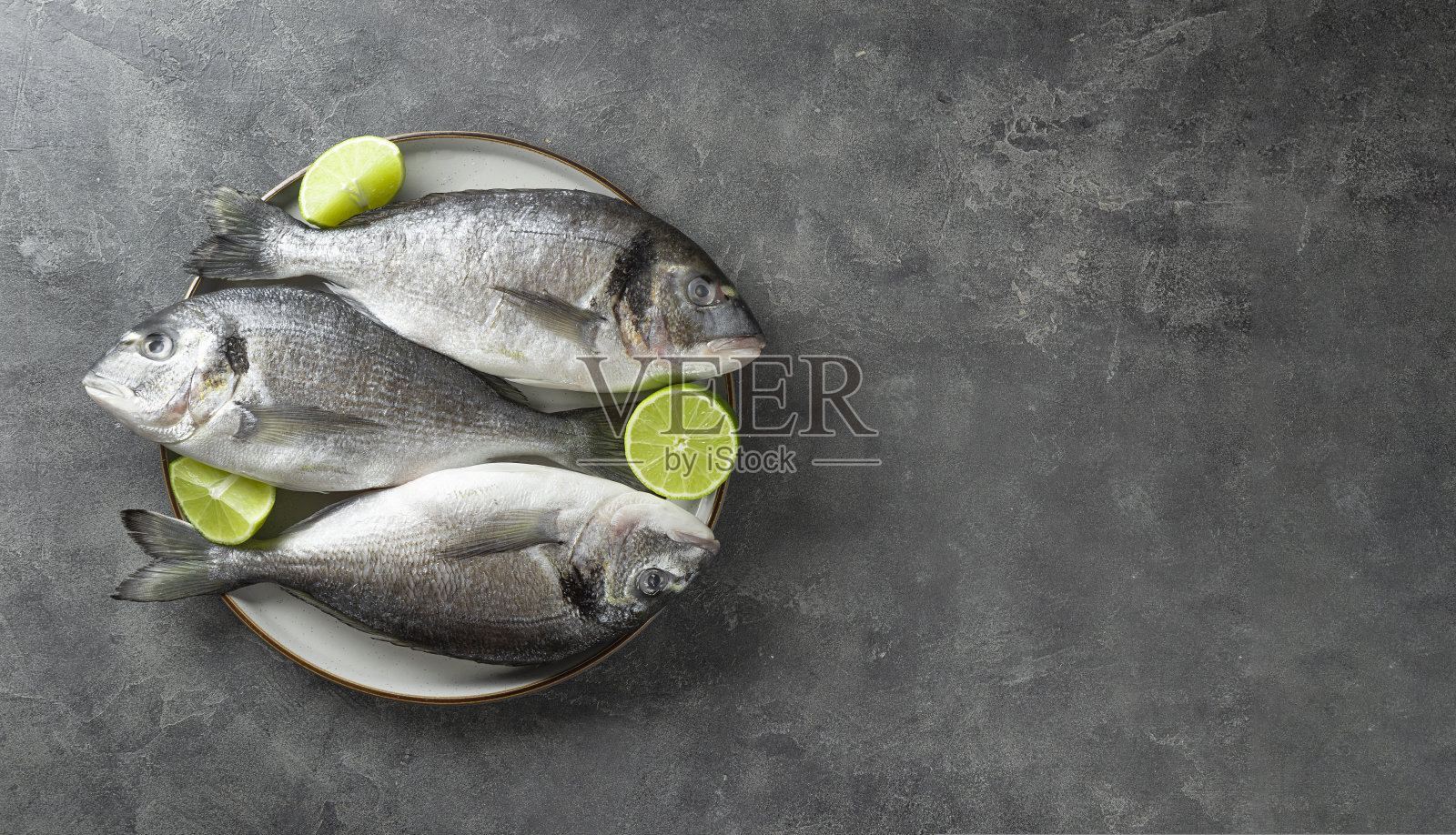 生多拉多鱼与青柠在盘子和灰色的背景上，俯视图。极简主义的背景与海鲜复制空间的文本照片摄影图片