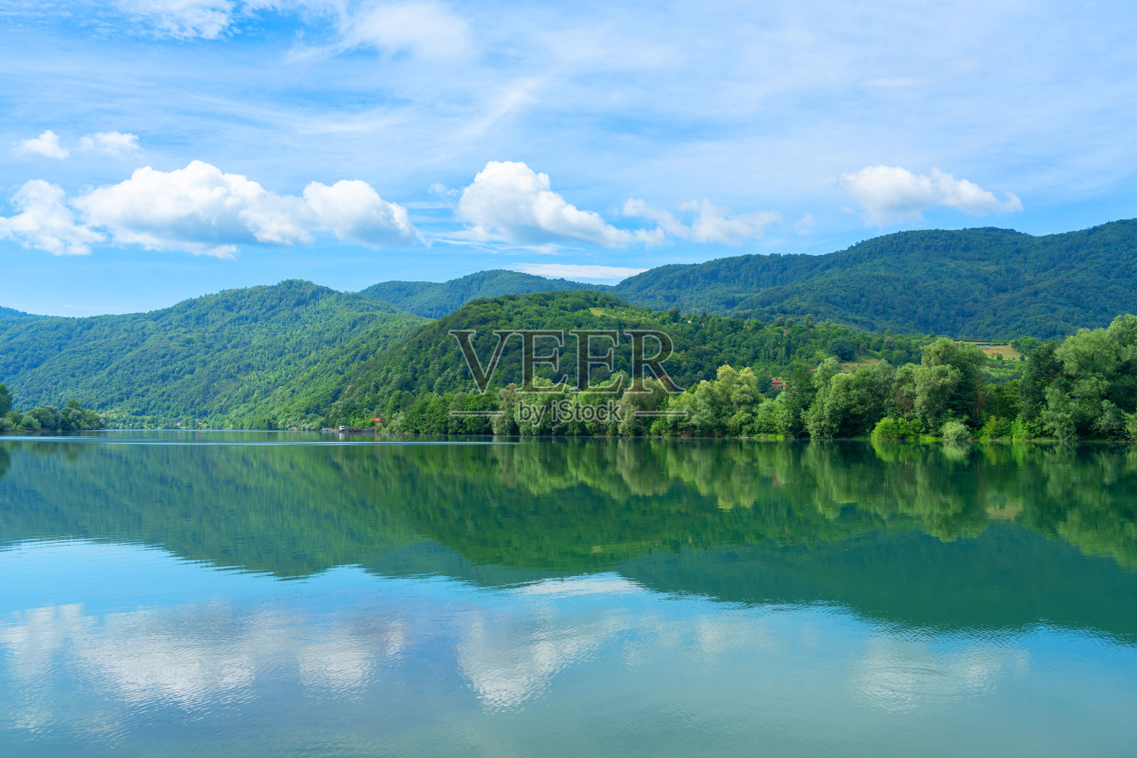 河岸被森林覆盖，水中倒映着云朵照片摄影图片