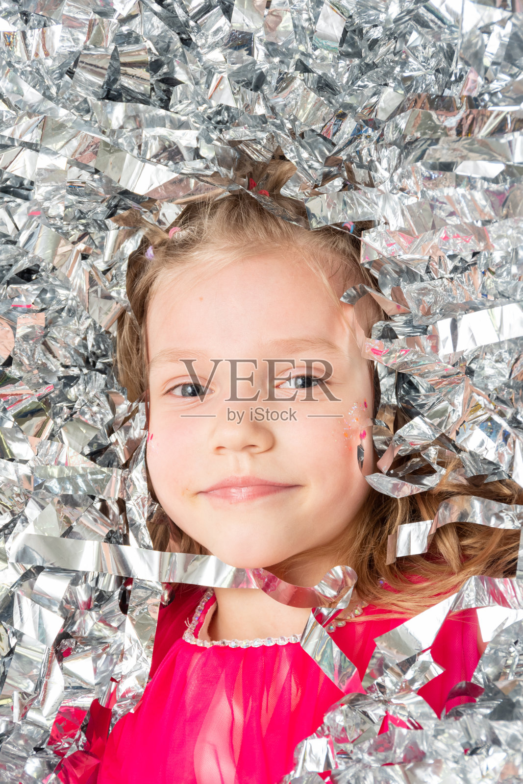 一个微笑开朗的女孩在一大堆银箔纸屑中，特写。穿着闪闪发光的亮片的女孩。照片摄影图片