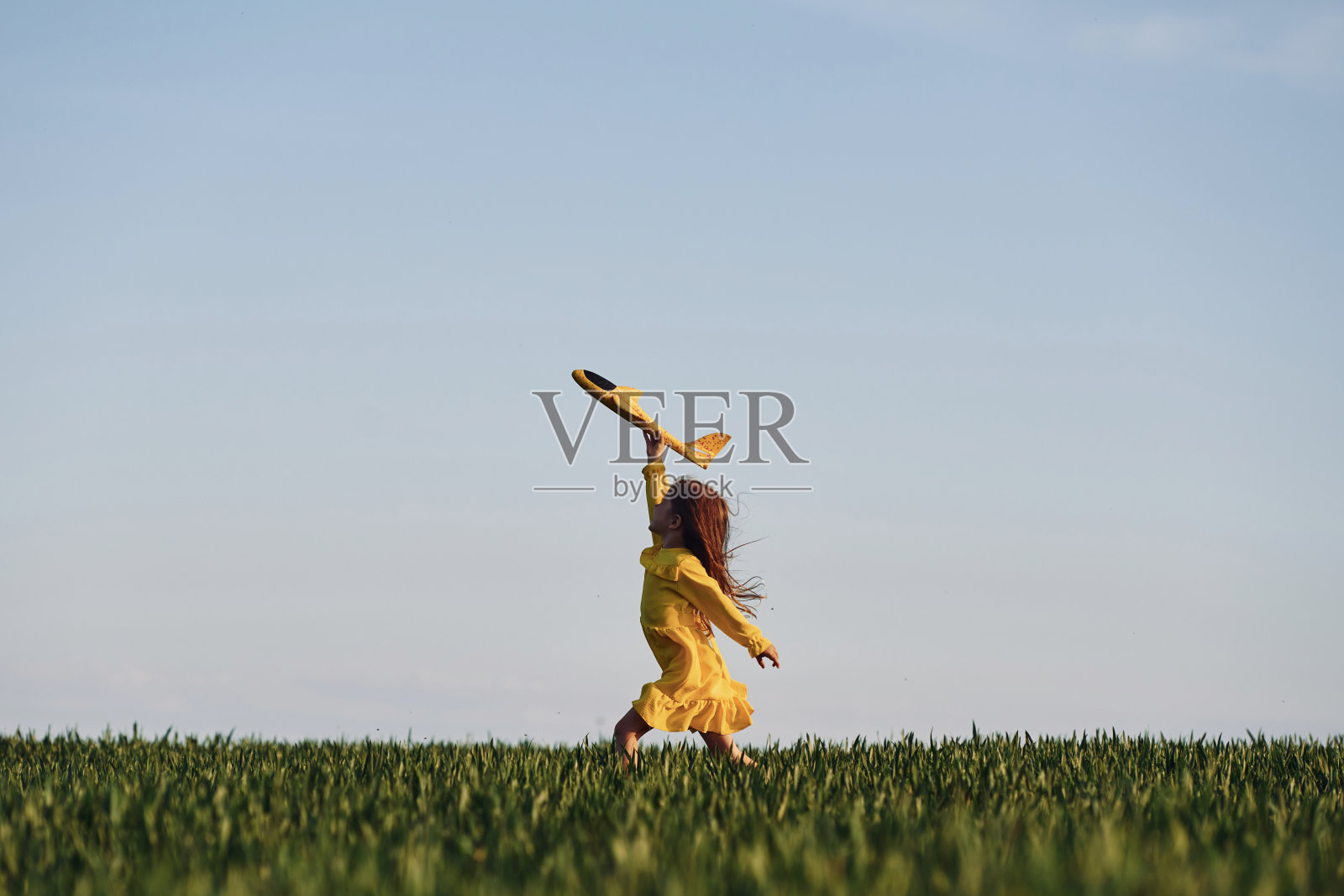 黄色的玩具飞机和衣服。快乐的女孩在夏天在户外的田野上散步照片摄影图片