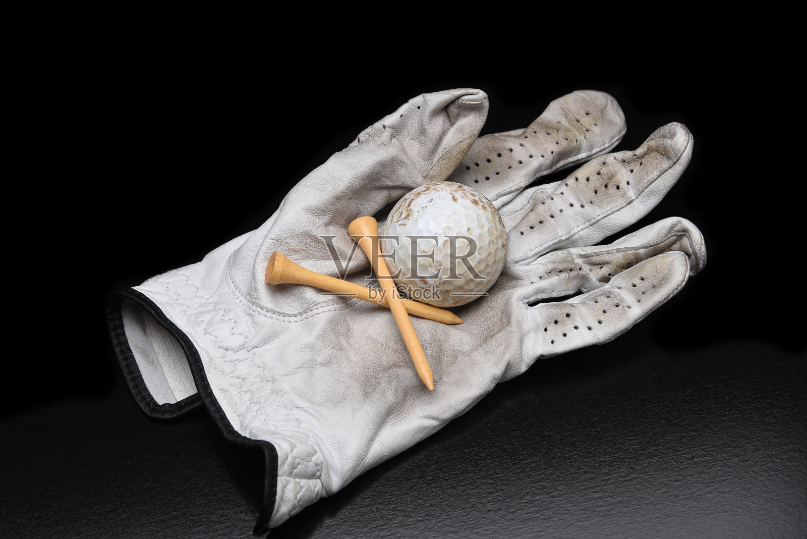 高尔夫静物。一副用过的高尔夫球手套，上面有球座和黑色的带有复制空间的脏高尔夫球。照片摄影图片