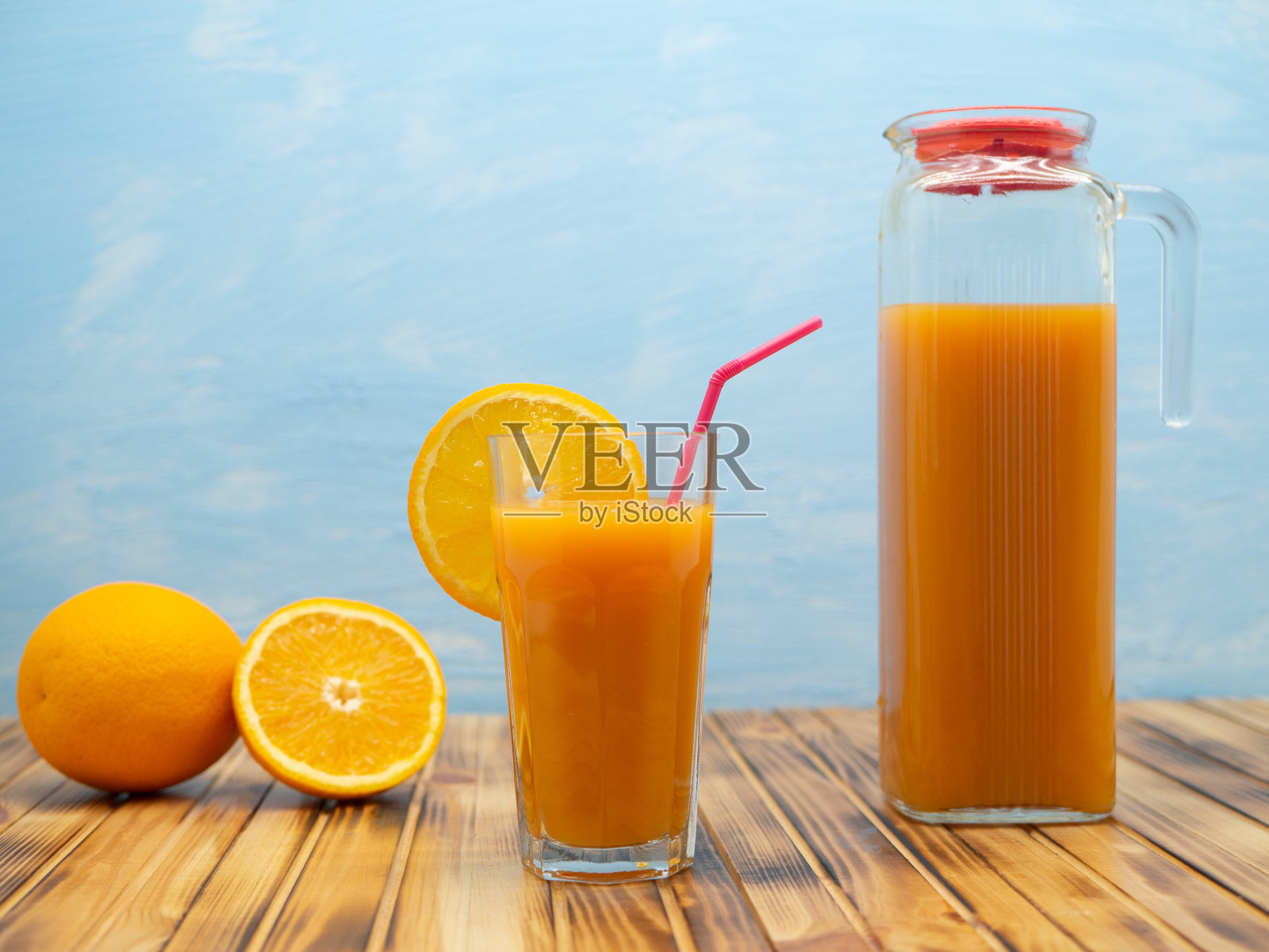 蓝色背景的木桌上放着玻璃杯和一罐橙汁。照片摄影图片