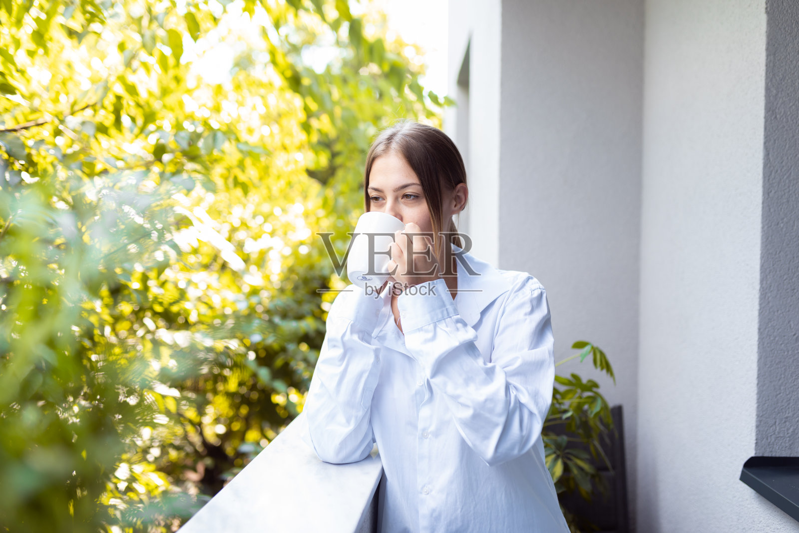 穿着白衬衫的年轻女子在有树的露台上喝咖啡照片摄影图片