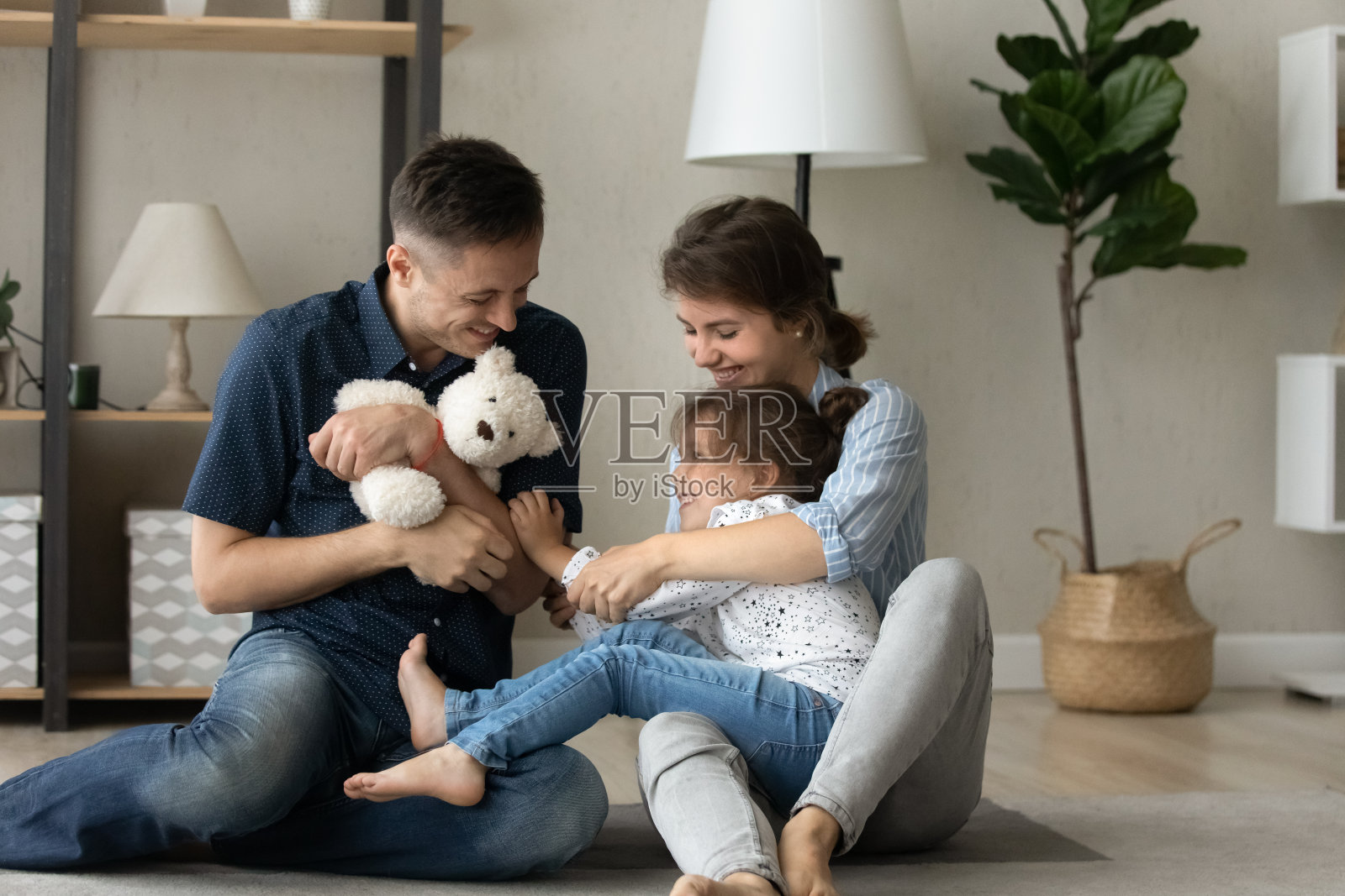 快乐的年轻父母和小女儿玩玩具。照片摄影图片