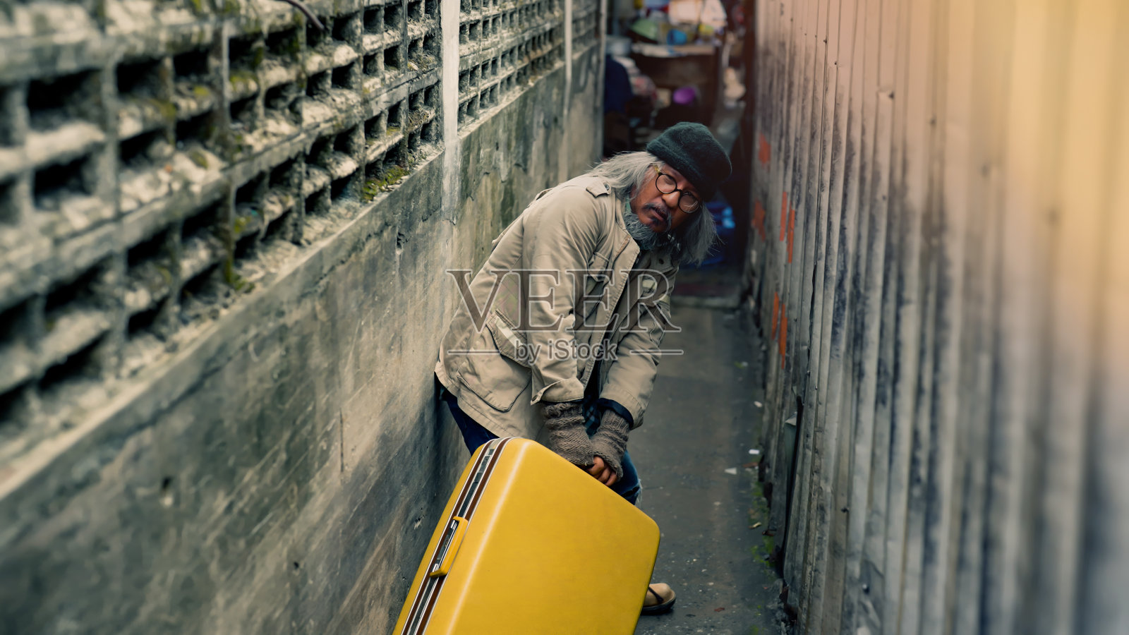 无家可归的亚洲男人在狭窄的小巷里拖着一个大 suitcase照片摄影图片