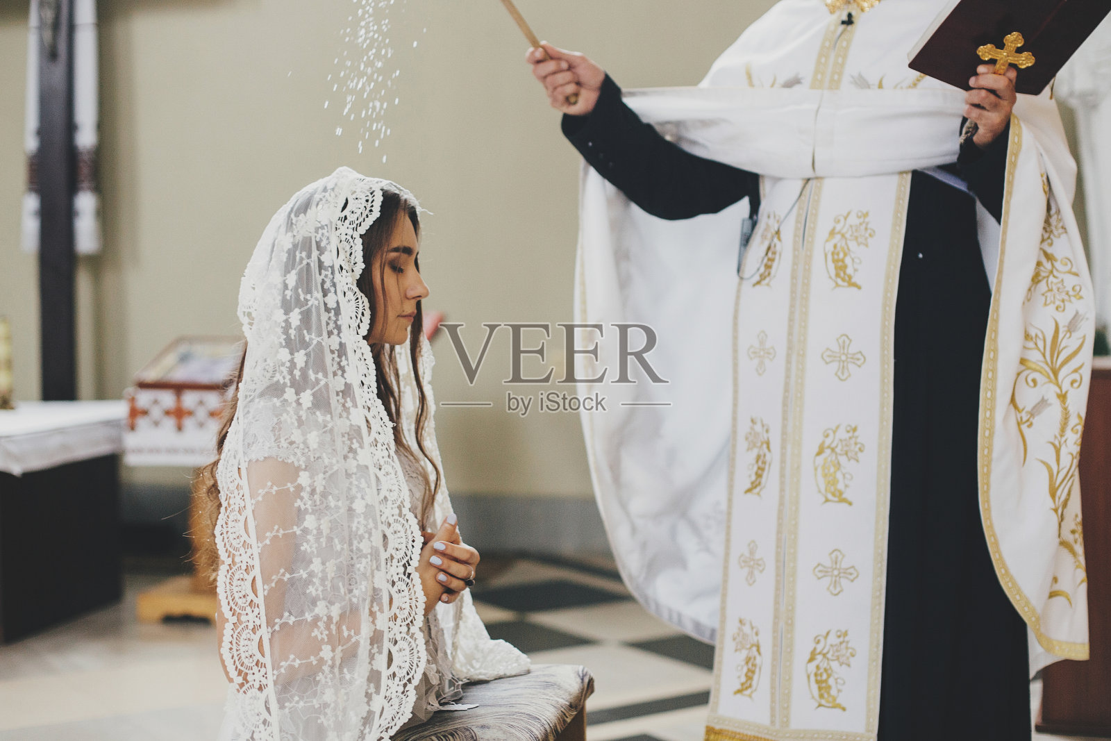 在教堂举行的神圣婚礼上，牧师在祭坛上用圣水和头巾祝福新娘。在大教堂举行婚礼。新娘祈祷的经典精神照片摄影图片