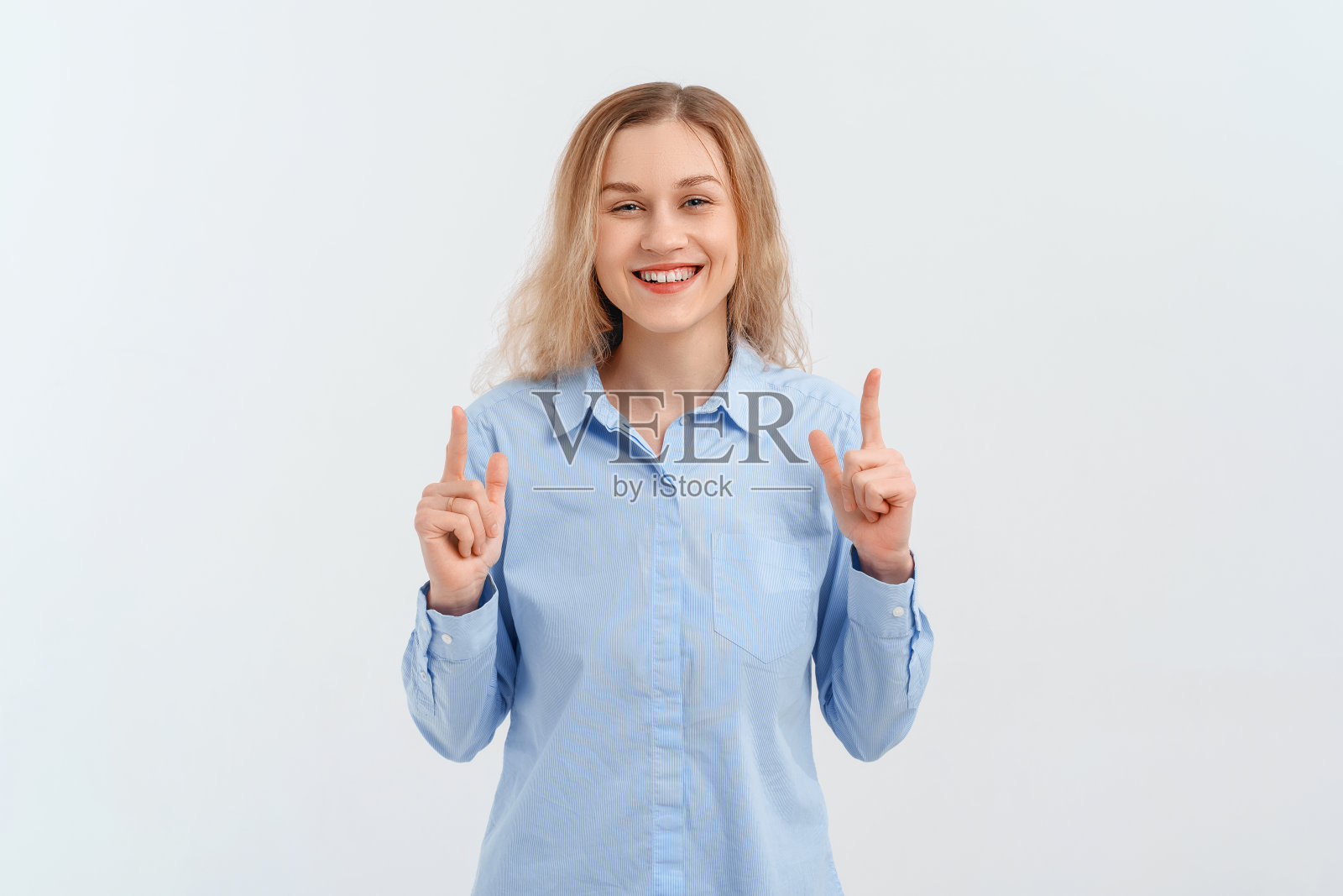 快乐兴奋的金发女孩用手比划着，手指向上，展示着最好的交易，展示着广告。室内工作室拍摄的白色背景照片摄影图片