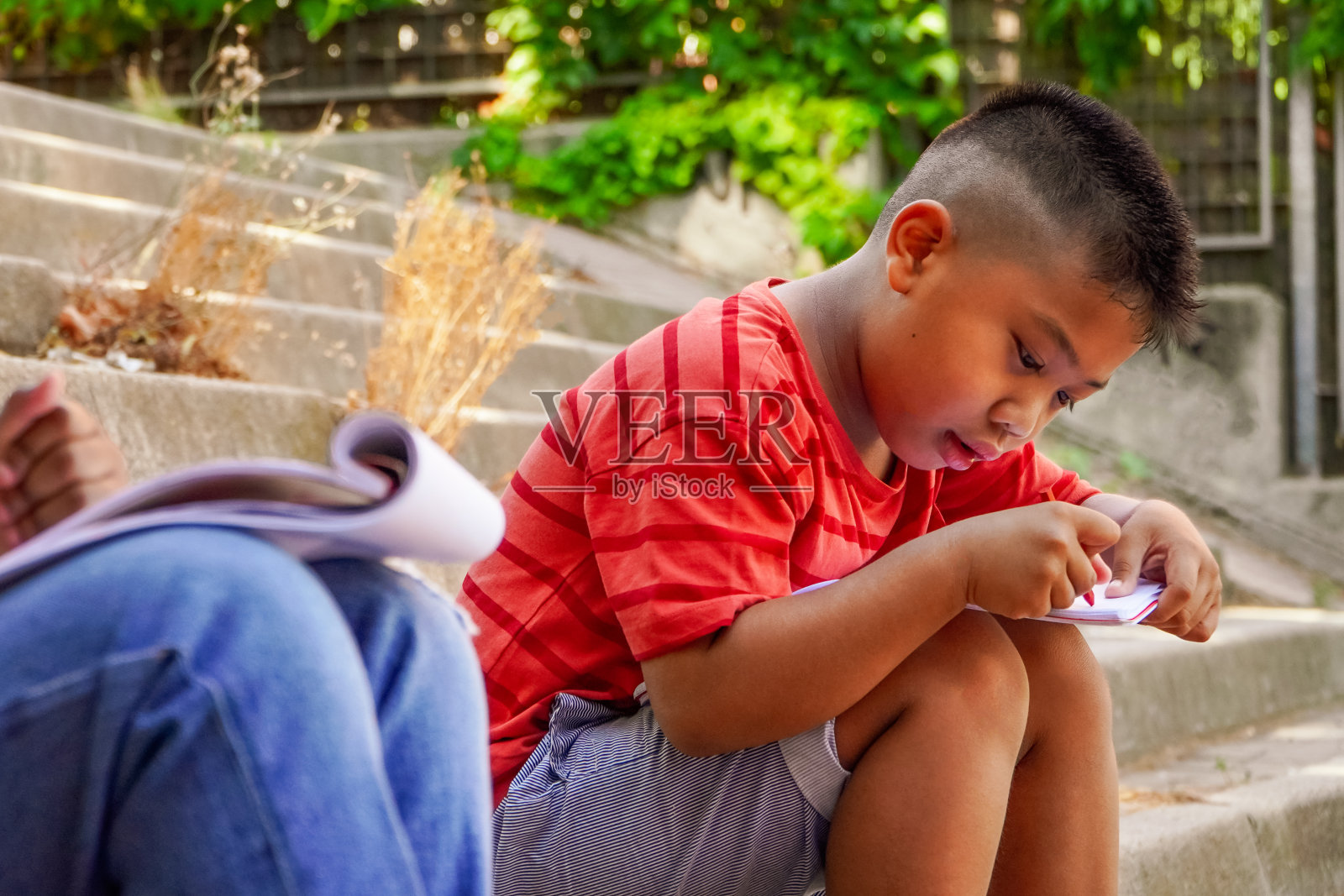 一个亚洲男孩在学校门口的楼梯上做作业。照片摄影图片
